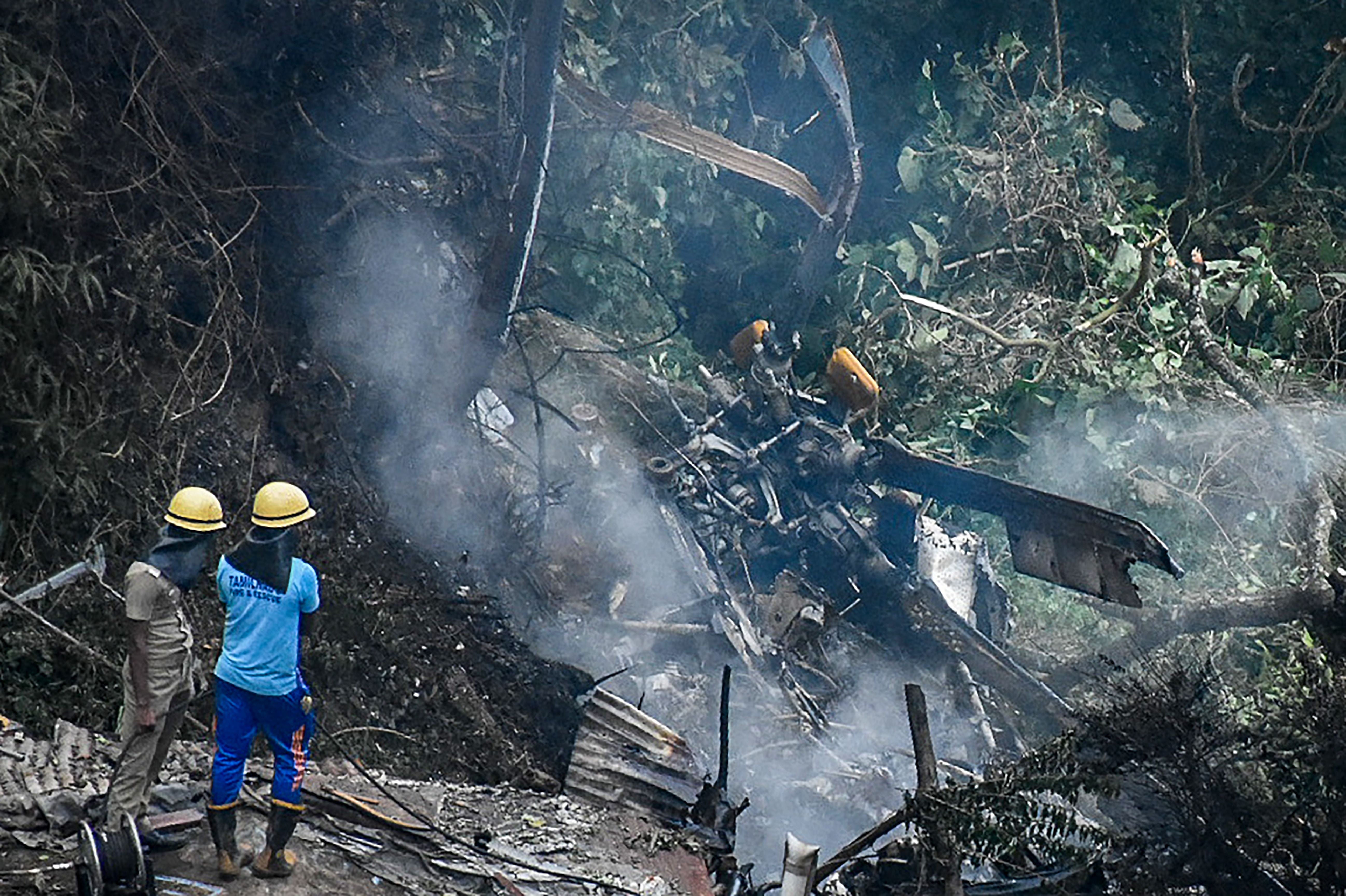 Firemen and rescue workers stand next to the debris of an IAF Mi-17V5 helicopter crash site in Coonoor, Tamil Nadu