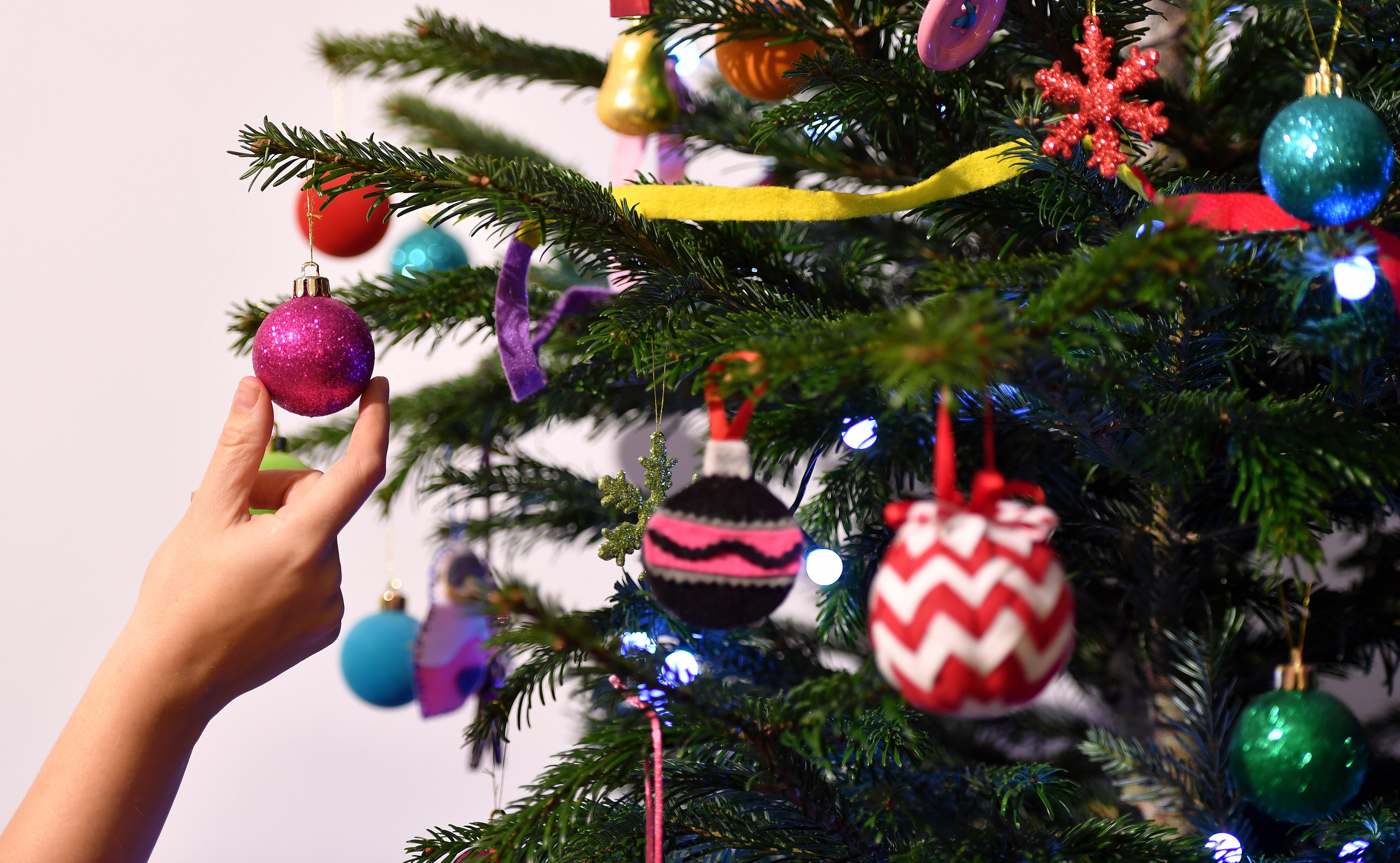 A woman adjusts a decoration on a Christmas tree.