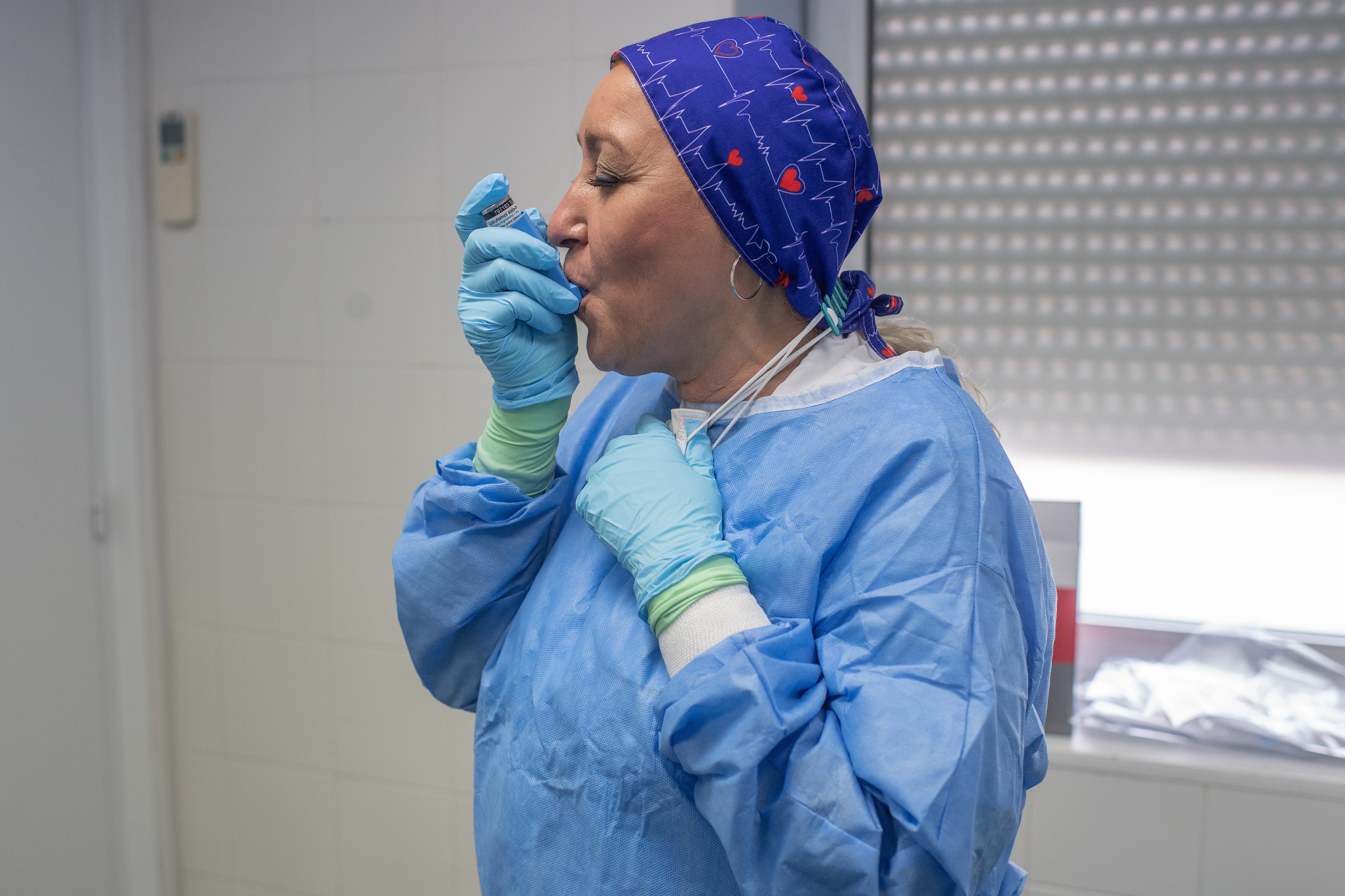 Primary health care nurse Mari Paz takes an asthma inhaler dose in between performing nasal swab