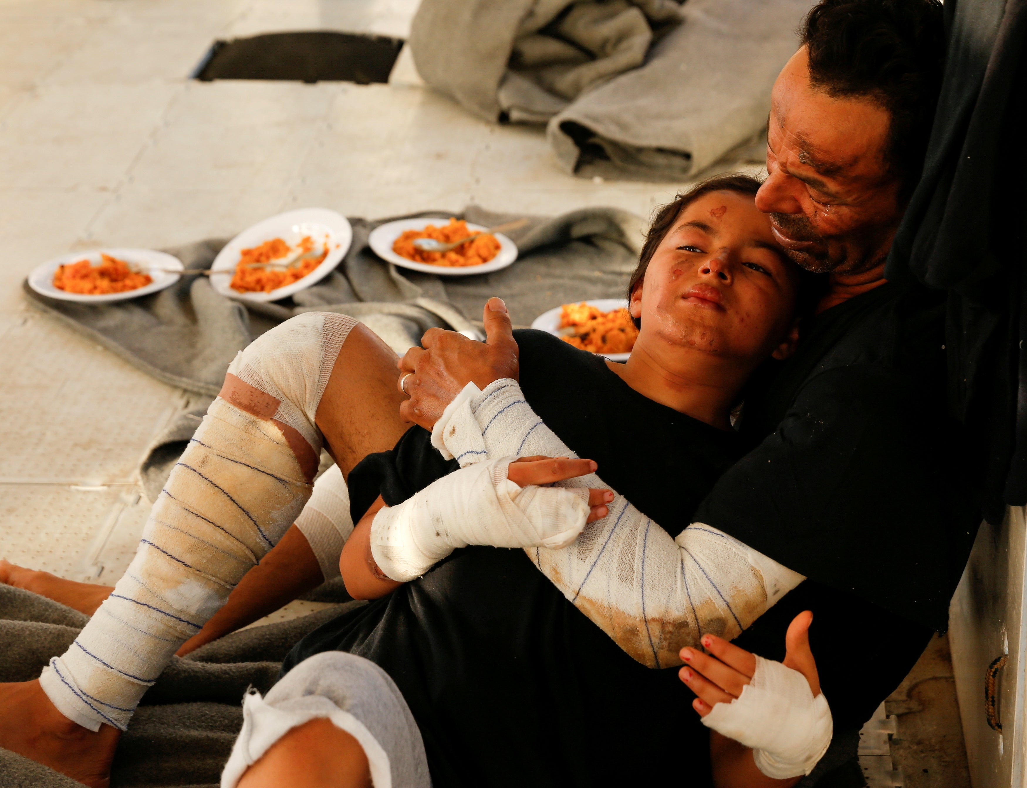 A Libyan man, who suffered severe burns while he fought a fire on a migrant boat, and his daughter, also injured in the fire, wait to be taken to safety off the coast of Lampedusa in the Mediterranean