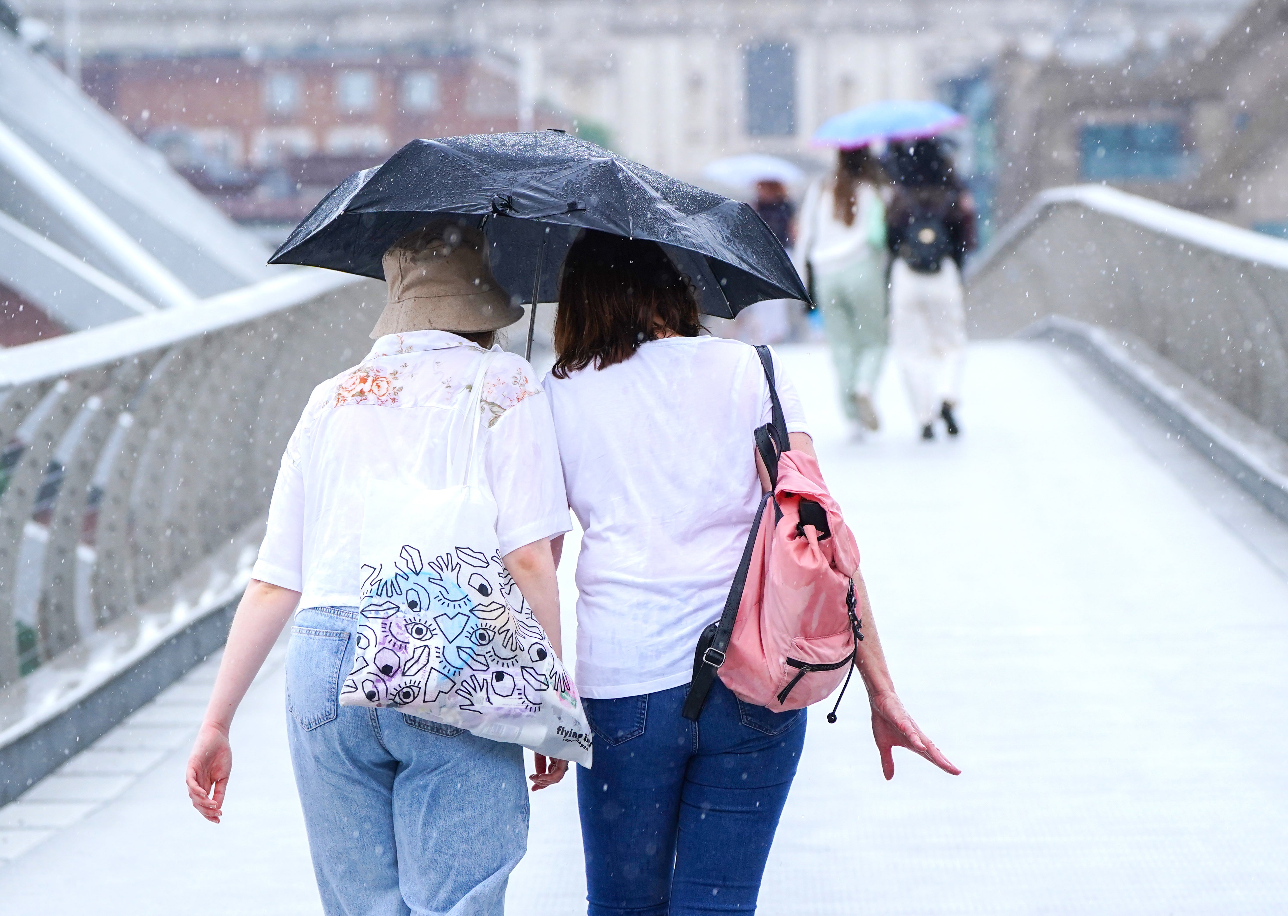 People on the Millennium Bridge in London during a rain shower (Ian West/PA)