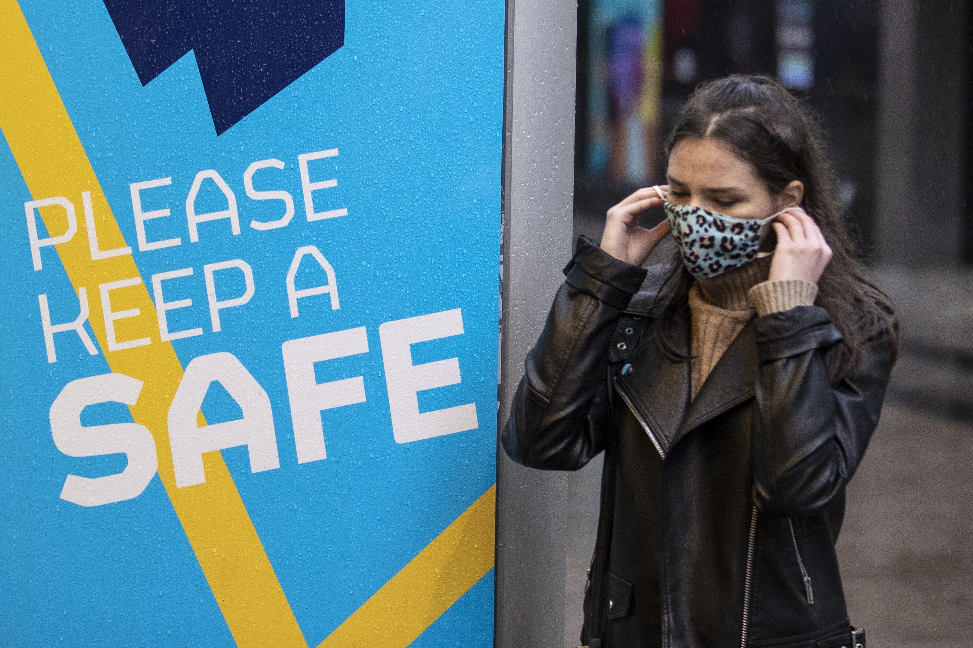 A young woman in Belfast puts on her face covering as she walks past a Covid-19 safety message from Belfast city council (Liam McBurney/PA)