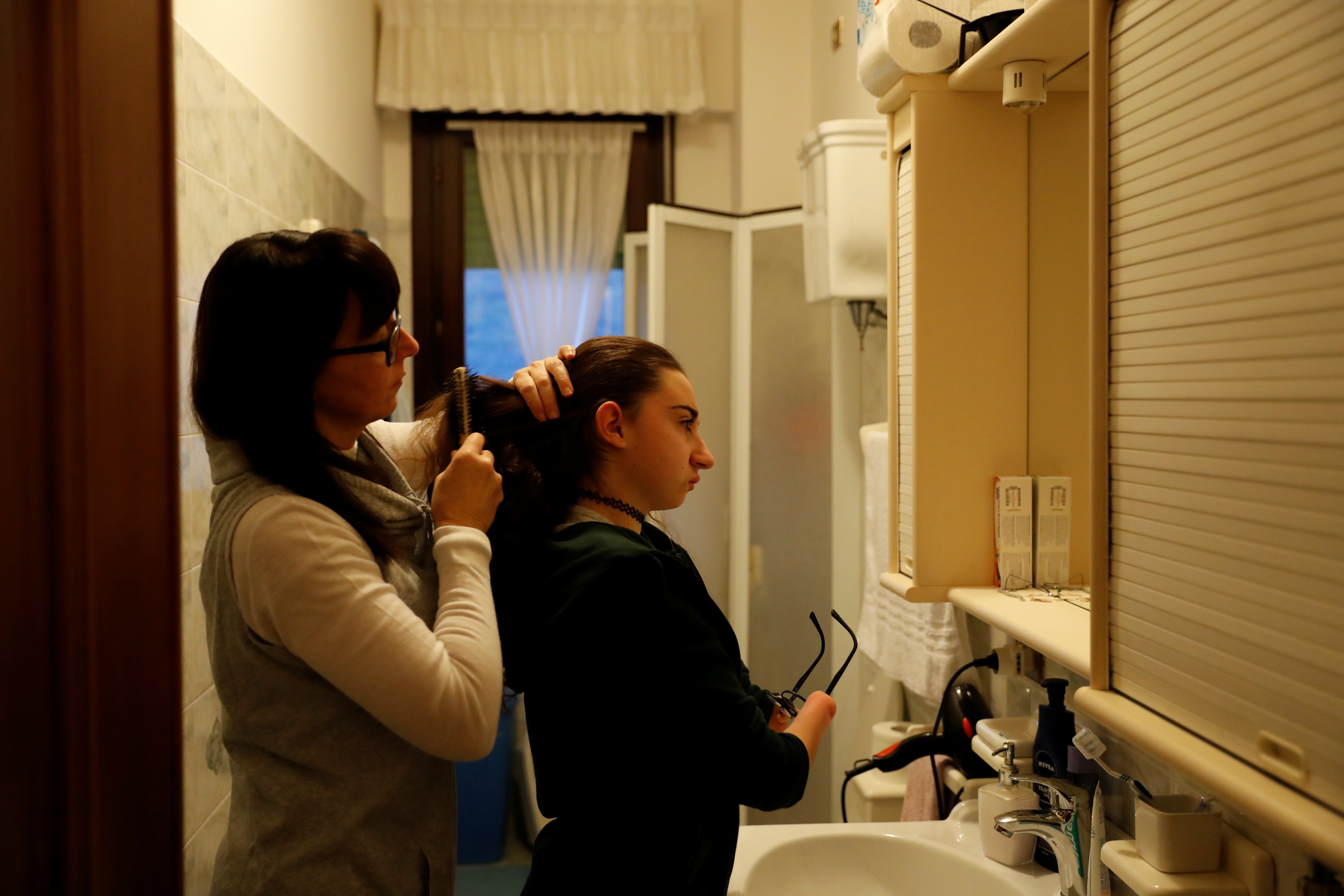 Francesca has her hair combed by her mother before going to school