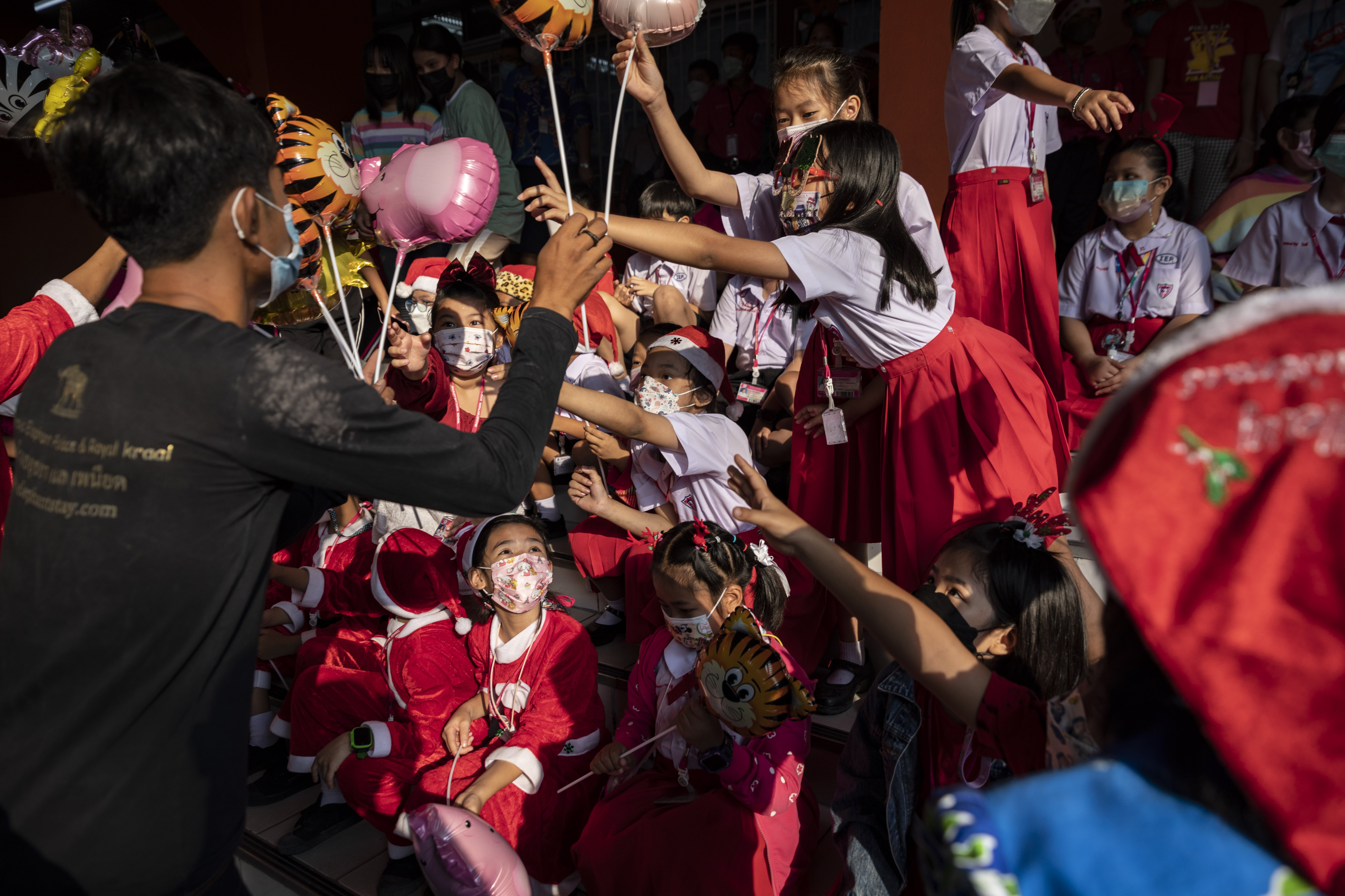 Elephants and their mahouts dressed as Santa Claus hand out balloons, hand sanitizer and other small gifts to schoolchildren