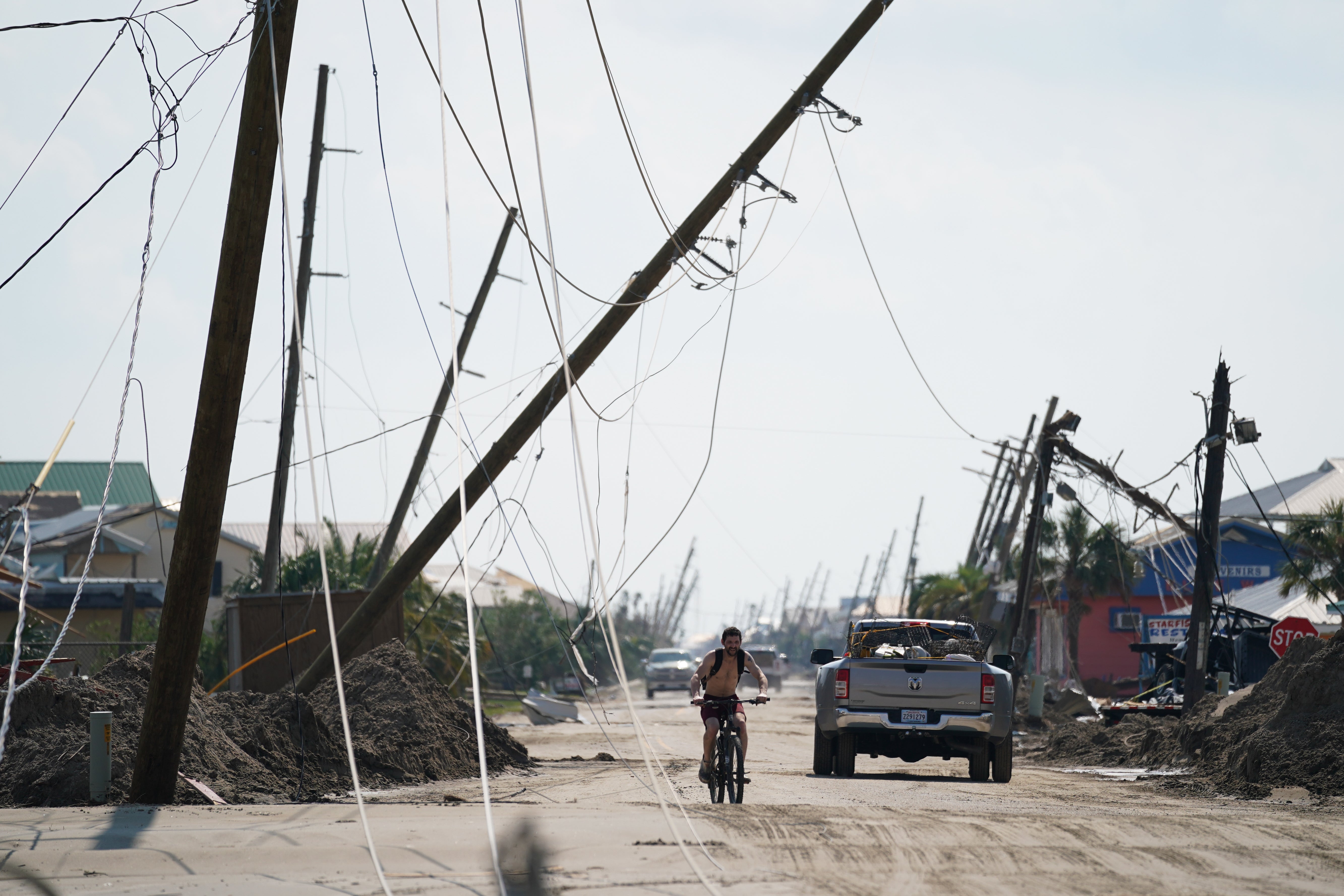 A man rides a bicycle on a road covered in sand in the wake of Hurricane Ida on September 3, 2021 in Grand Isle, Louisiana