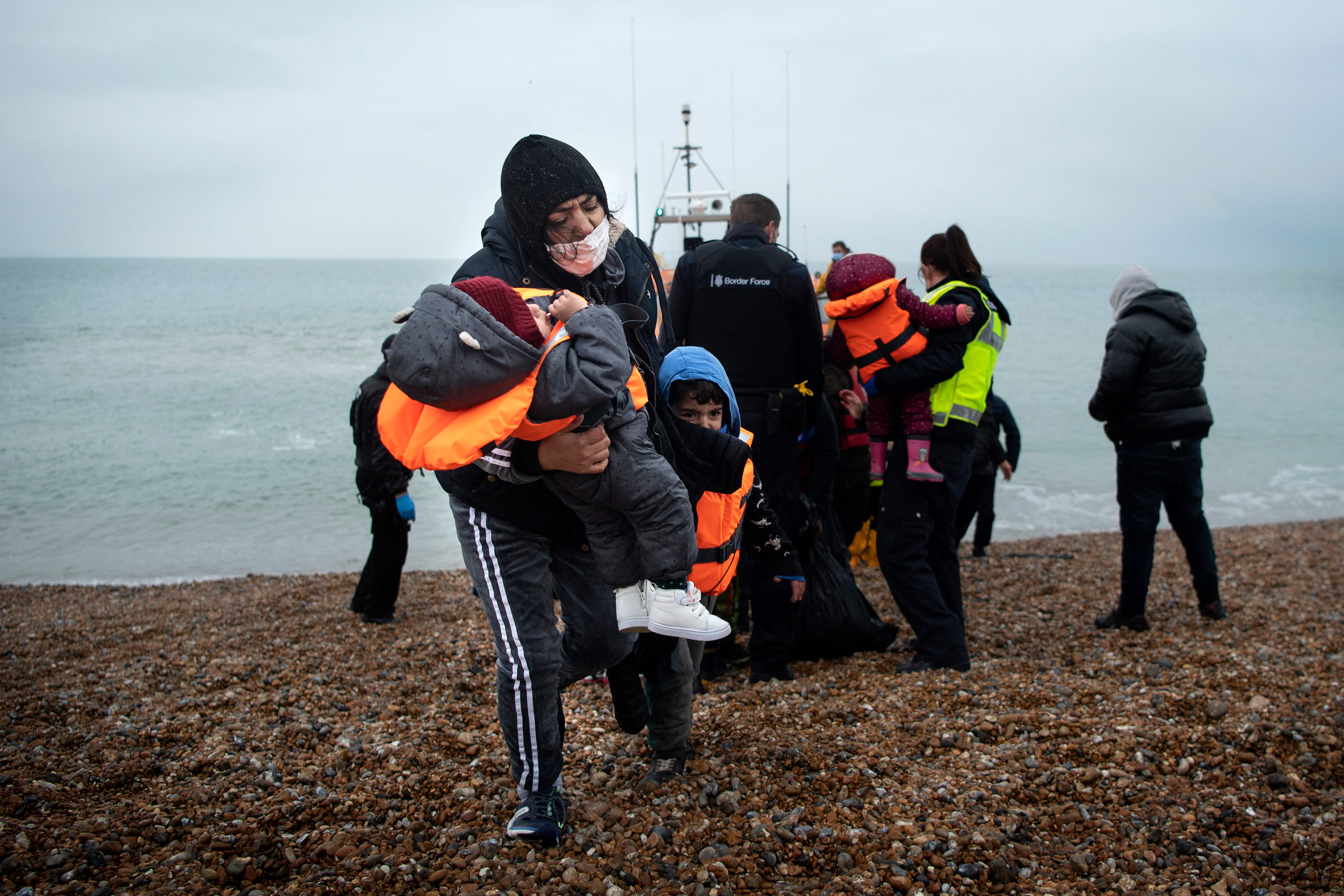 A migrant carries her children after being helped ashore from a RNLI lifeboat at a beach in Dungeness