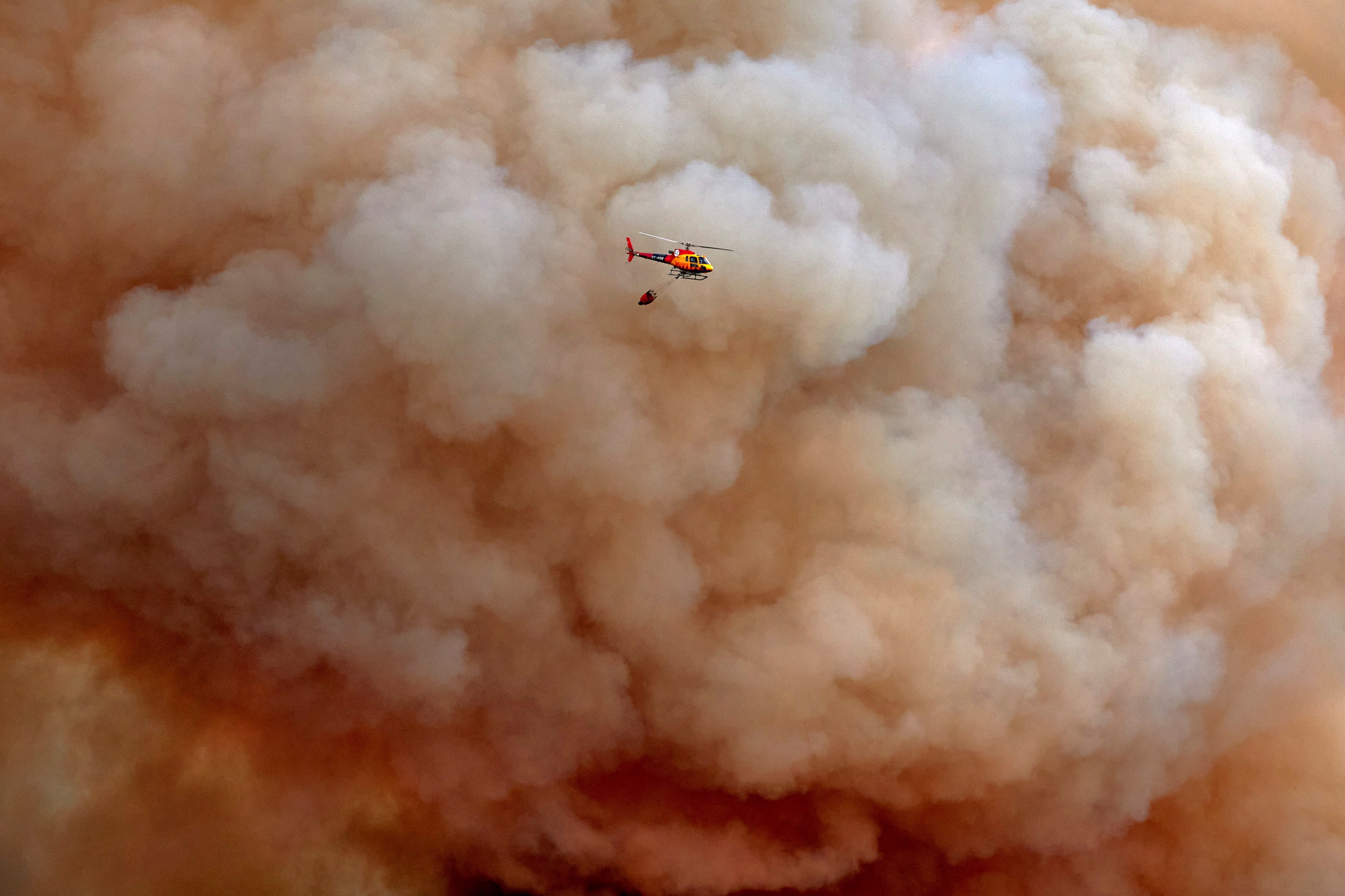 A helicopter pours water onto the forest fire originated in Girona, Spain