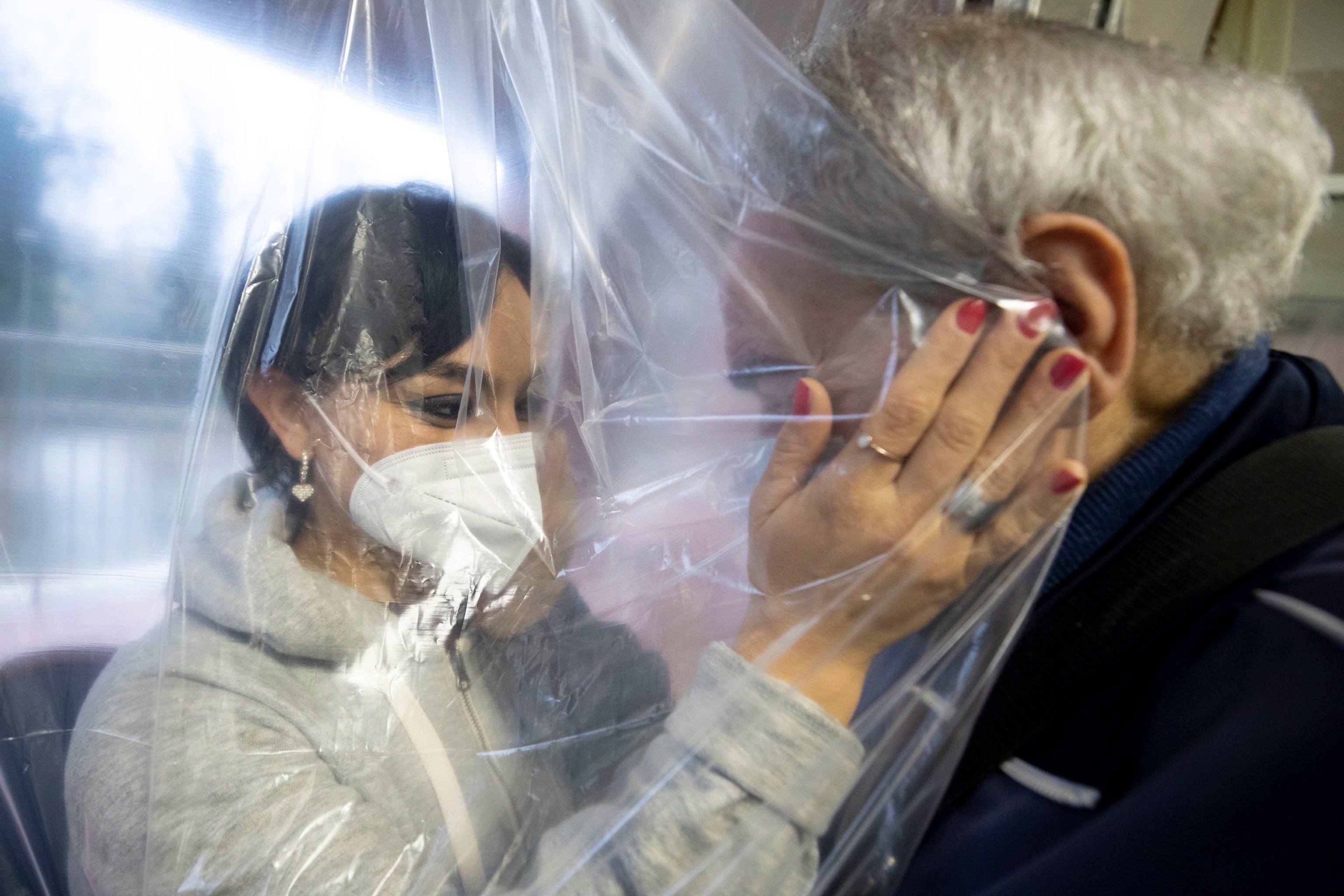 A woman wearing a face mask touches the face of an elderly patient of a nursing home through a special curtain, in Rome, Italy