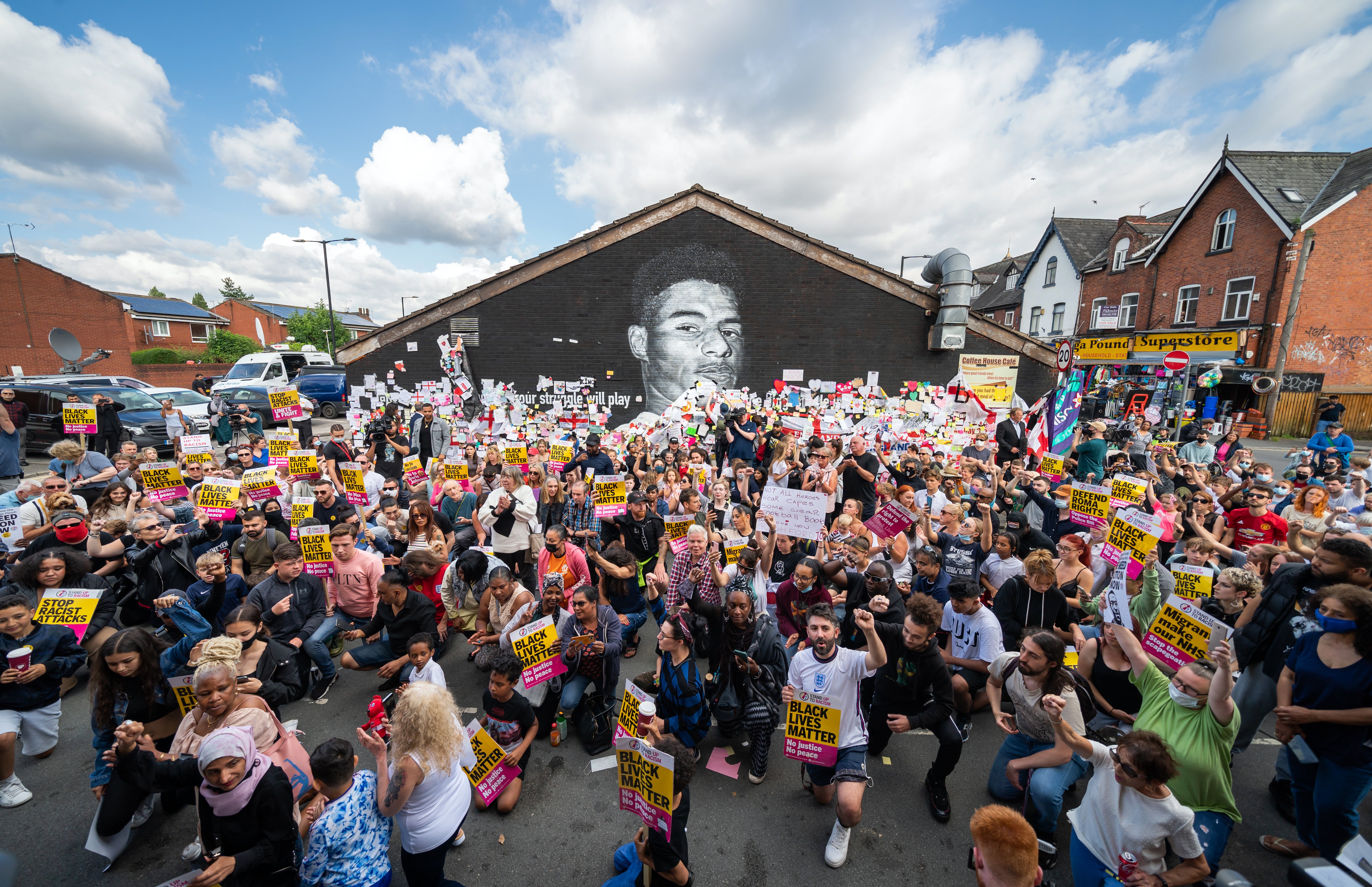 People take the knee in support of England football player Marcus Rashford in front of his mural on Copson Street, Withington