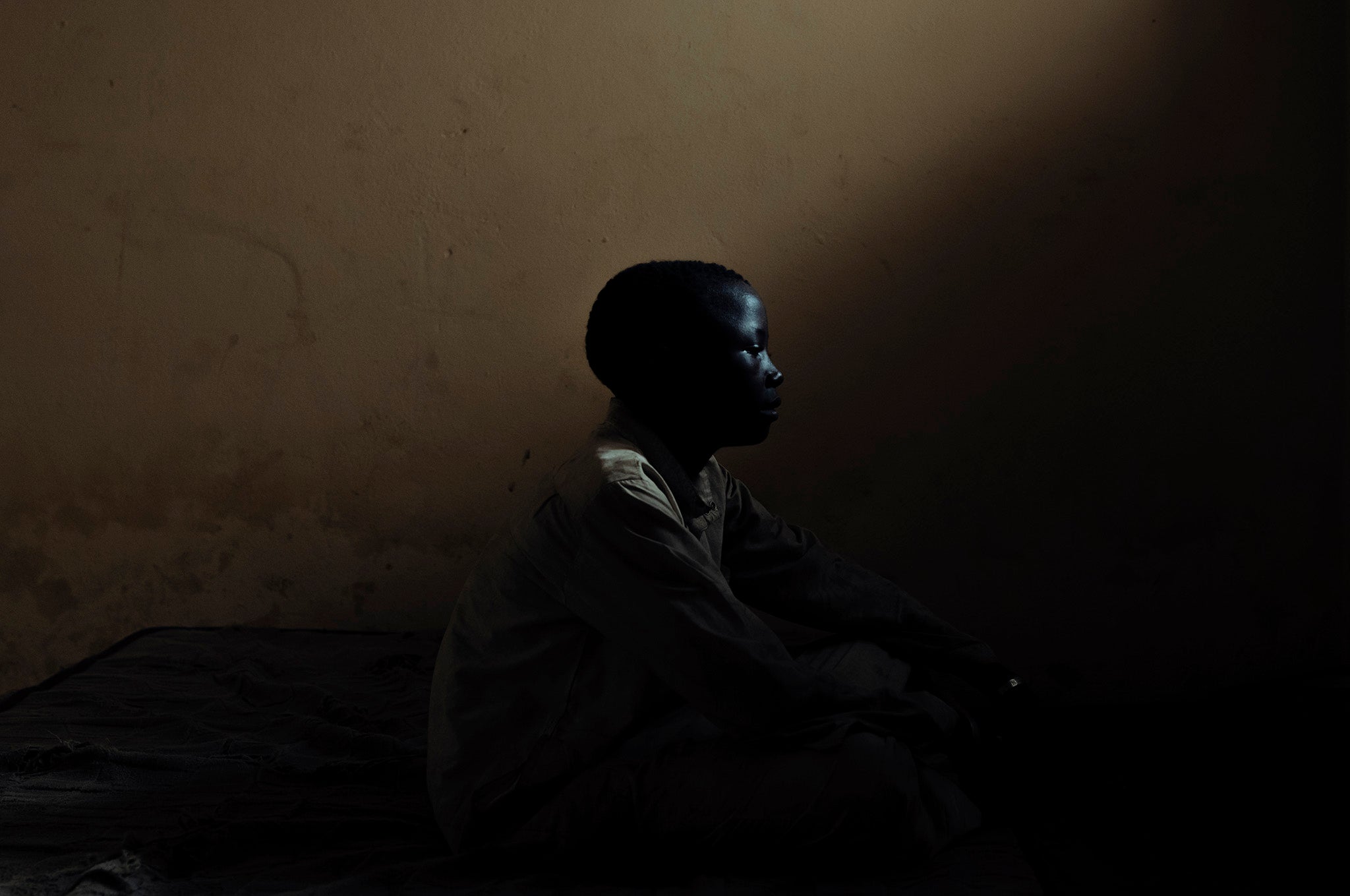 A child registered at a religious school in Bamako, Mali, sits in silence and solitude in a darkened room with a small window