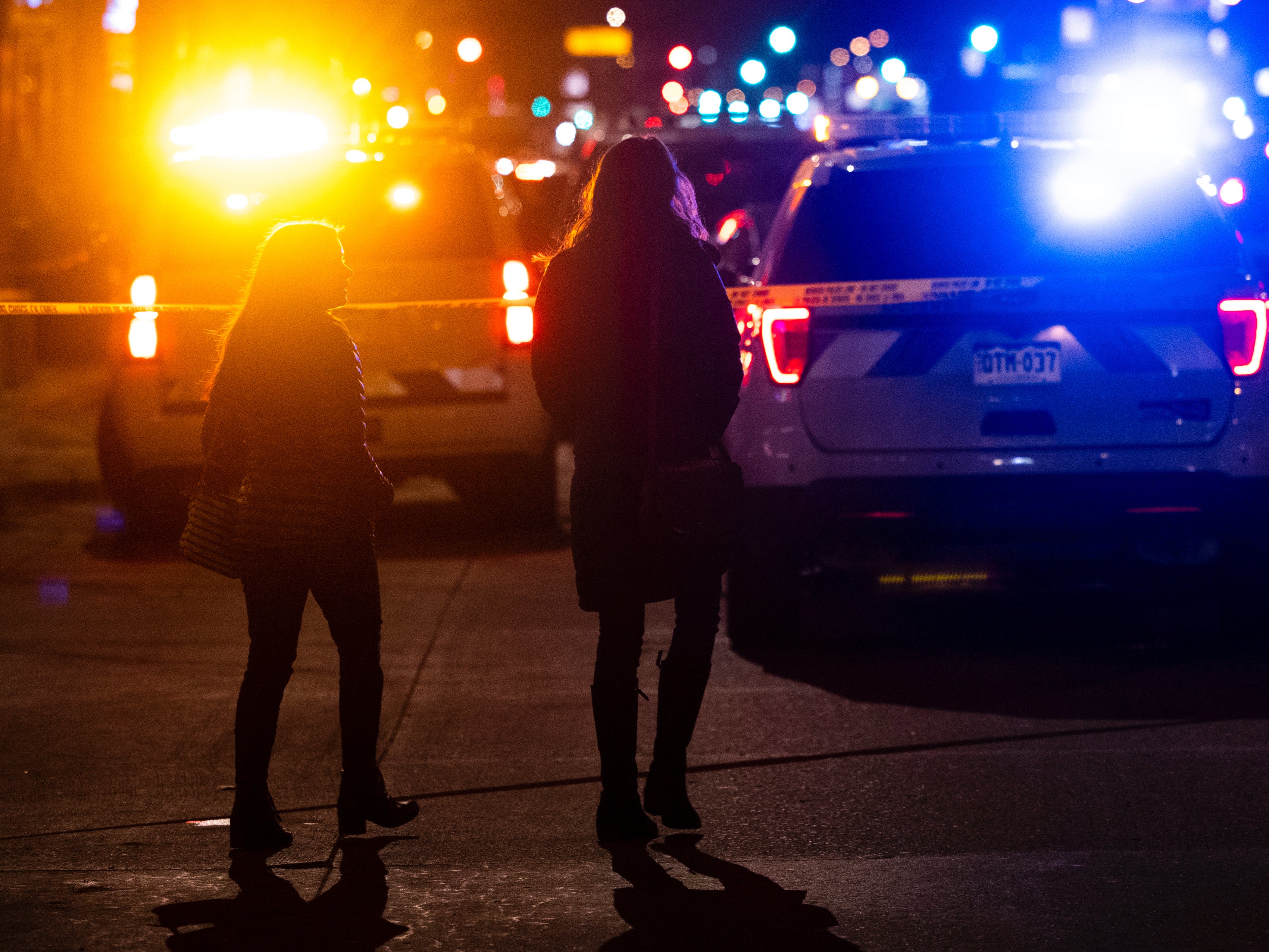 People walking past police cars parked outside a tattoo shop in Denver, Colorado, following a shooting spree