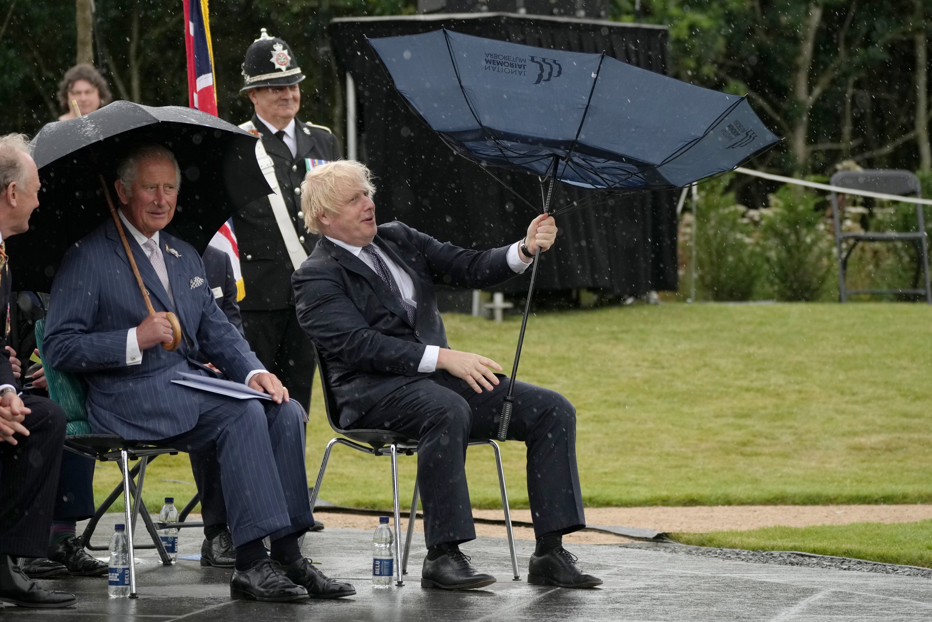 The Prince of Wales looks on as Prime Minister Boris Johnson struggles with an umbrella at the National Memorial Arboretum in Alrewas, Staffordshire