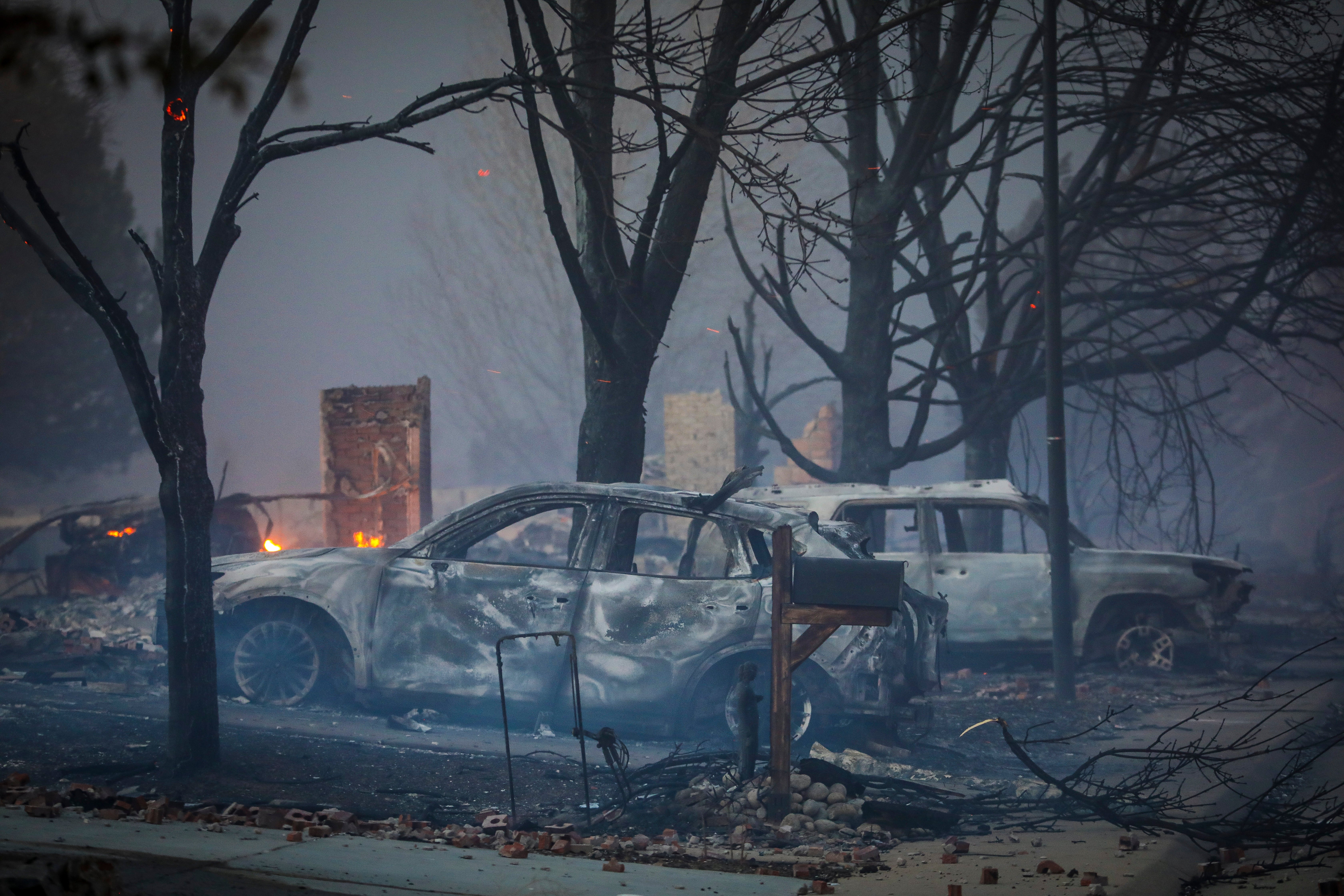 Burnt out vehicles sit amidst the smoke and haze after a fast moving wildfire swept through the area in the Centennial Heights neighborhood of Louisville, Colorado on 30 December 2021