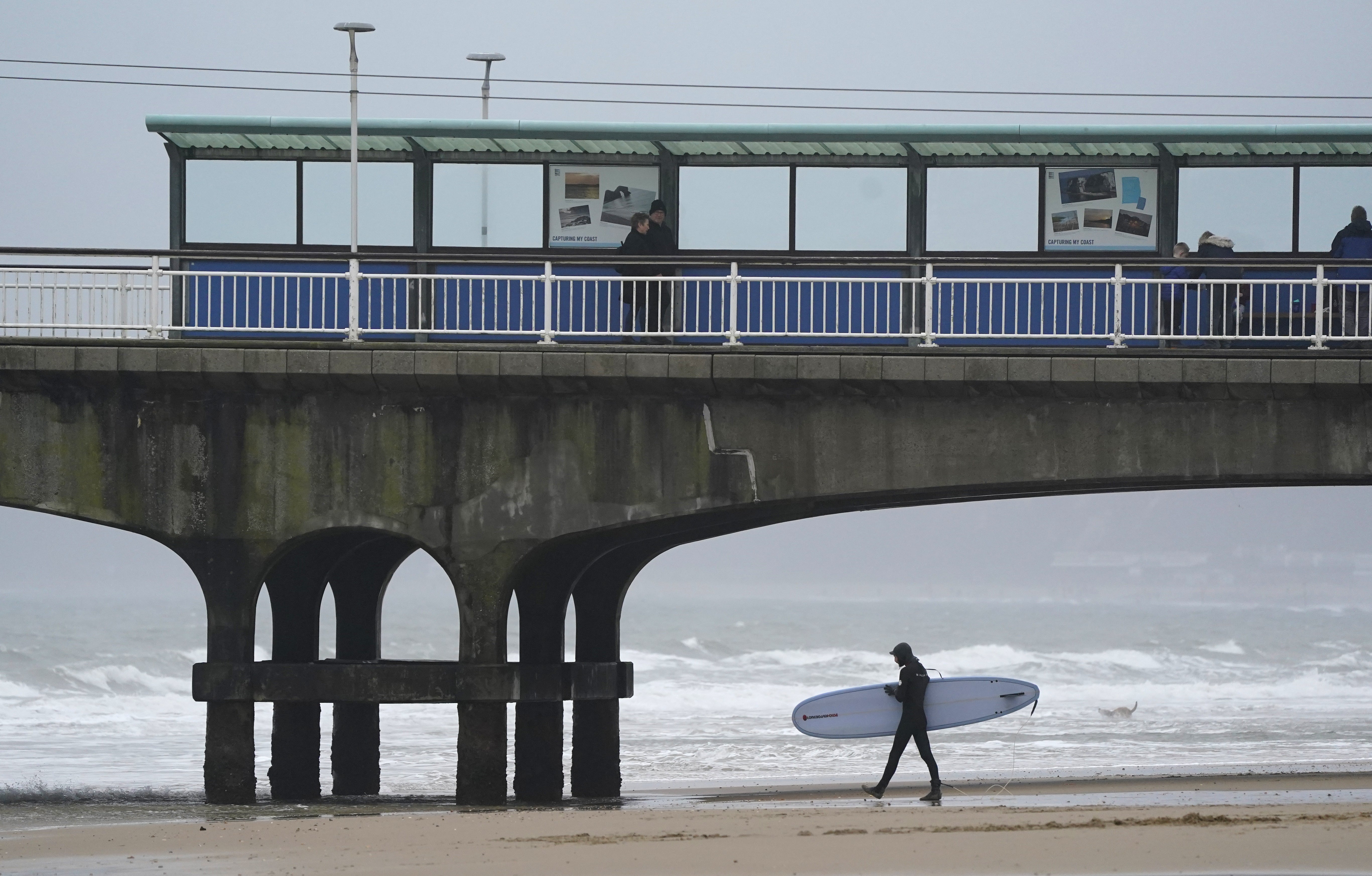 A surfer walks into the sea off Bournemouth beach in Dorset (PA)