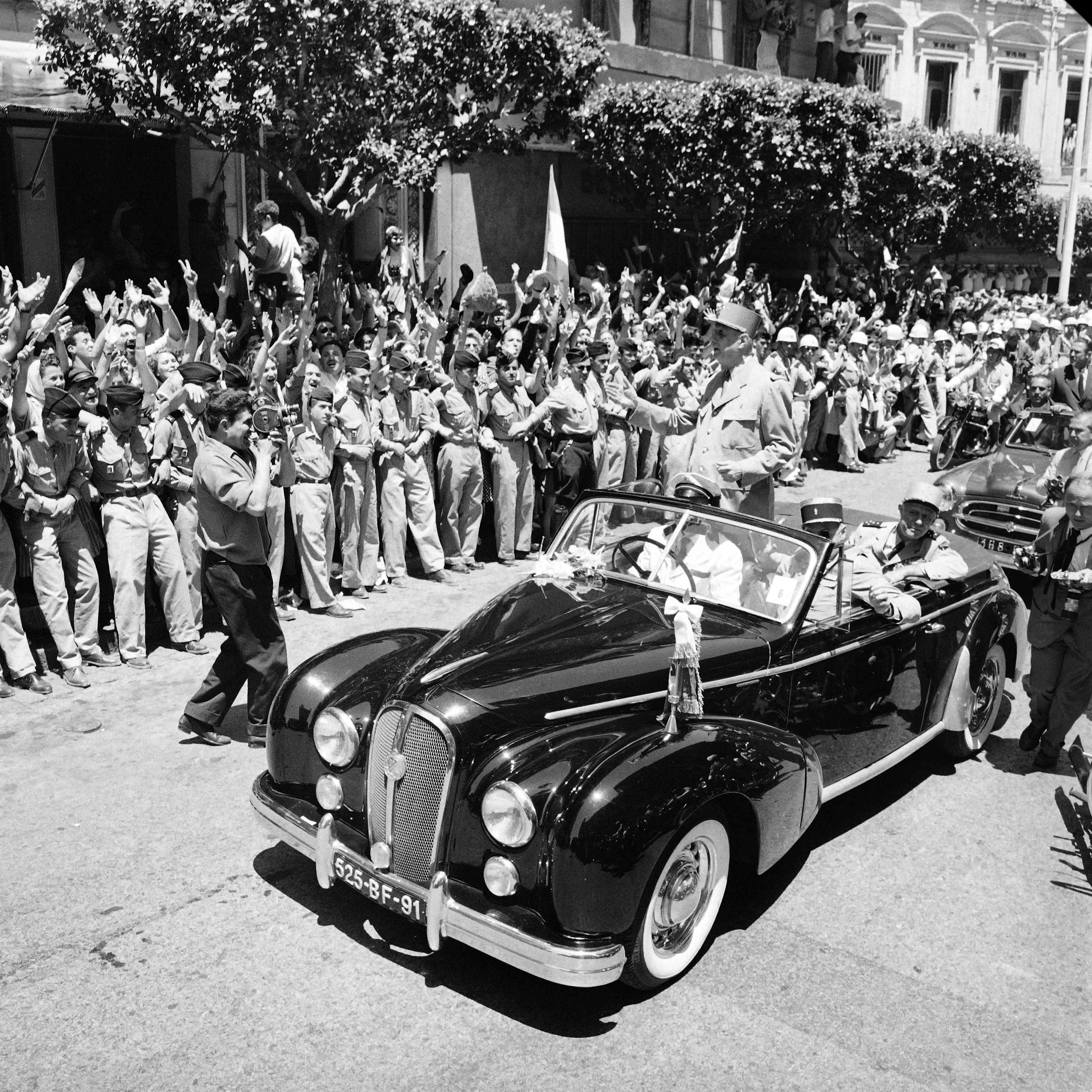 General Charles de Gaulle standing in an uncovered car, greets the cheering crowd in Algiers in June 1958