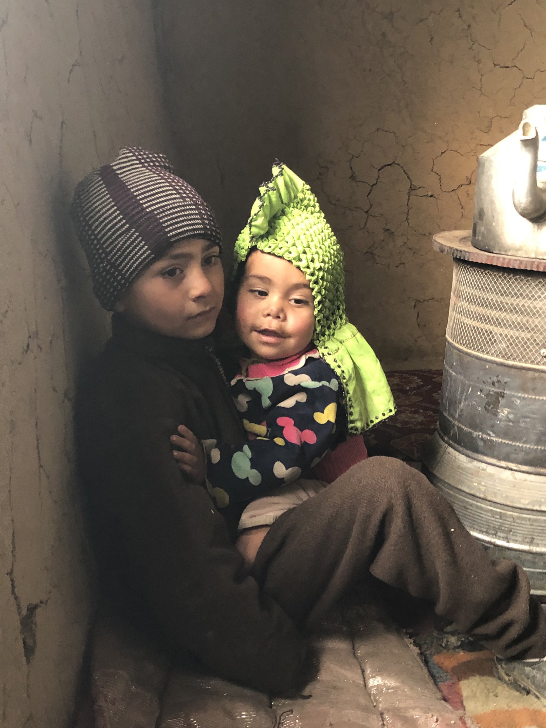 Beside a cold stove in their frigid two-room house in Kabul, a son of Mahmad Ewaz, a rural war refugee, tries to comfort his baby sister and keep her warm in Kabul