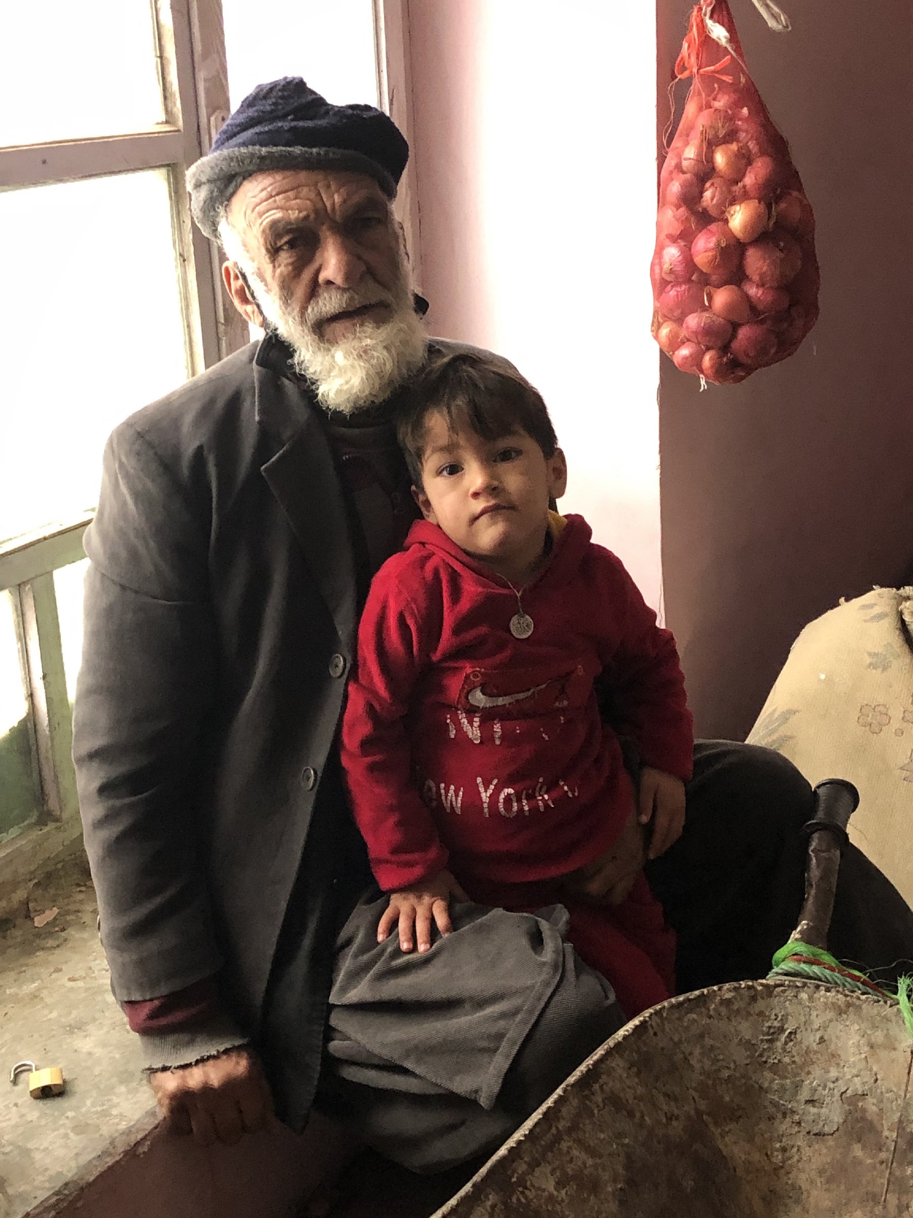 Abdul Hadi sits with his grandson Yasin and the wheelbarrow he pushes for hire