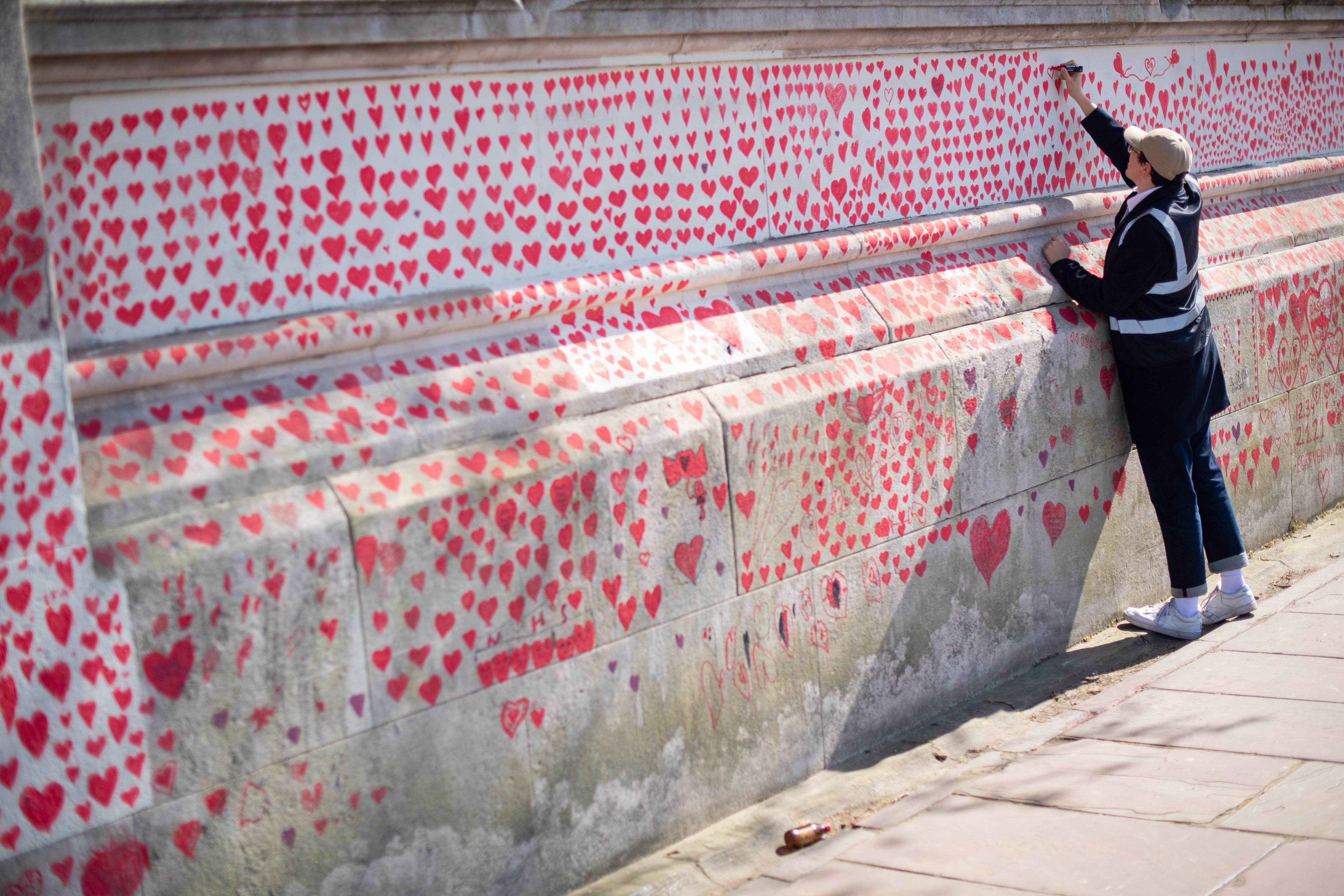 A volunteer adds hearts to the Covid memorial wall in Westminster, central London (Dominic Lipinski/PA)