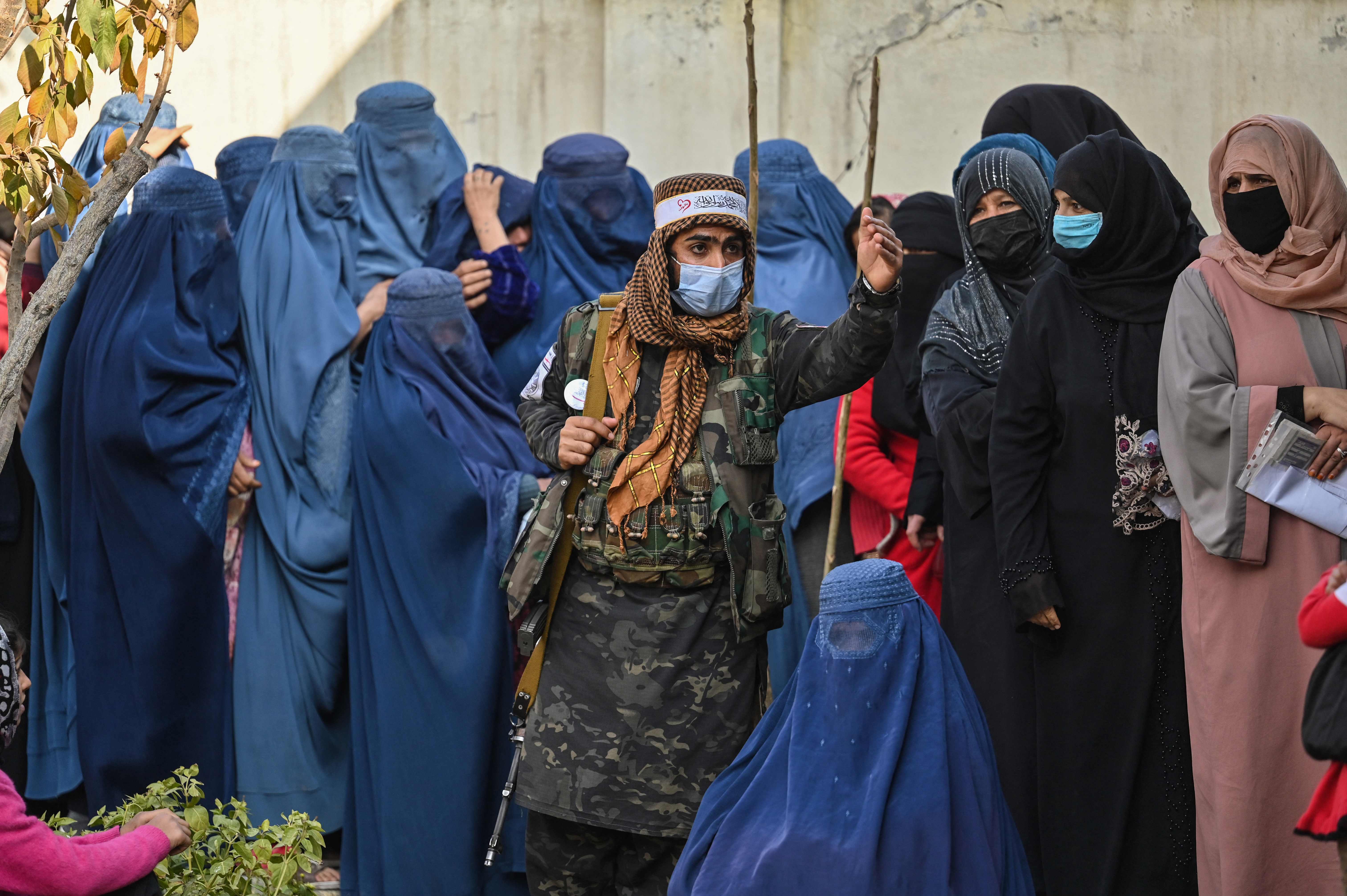 A Taliban fighter stands guard as women wait in a queue during a WFP cash distribution in Kabul