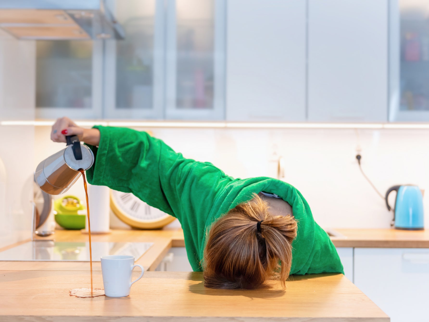 A tired woman pours coffee, misses the cup