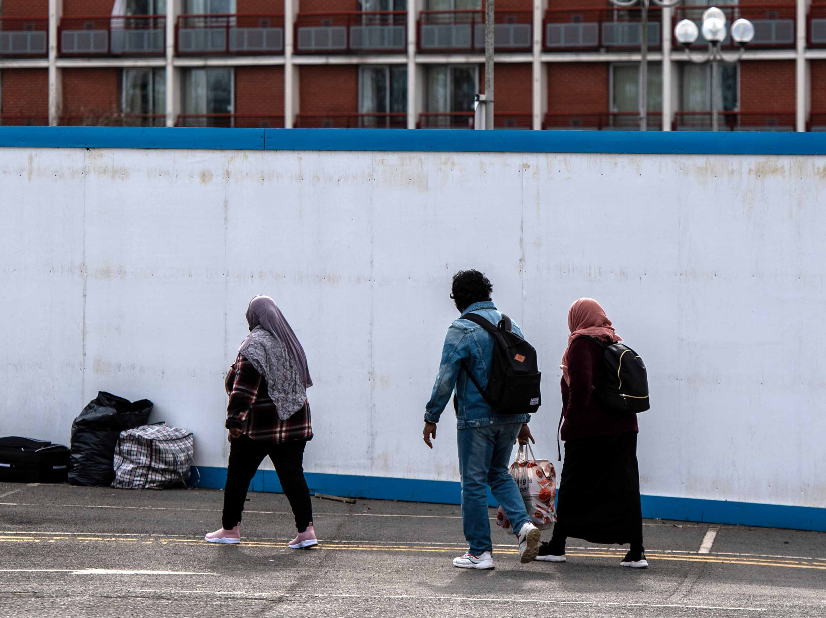 Asylum seekers enter the Crowne Plaza hotel in London through an exterior perimeter wall that was installed during their stay in February