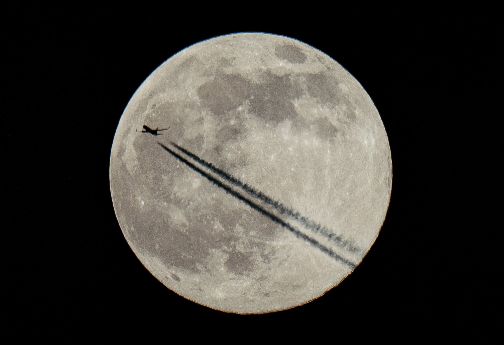 A plane flies past the moon over London