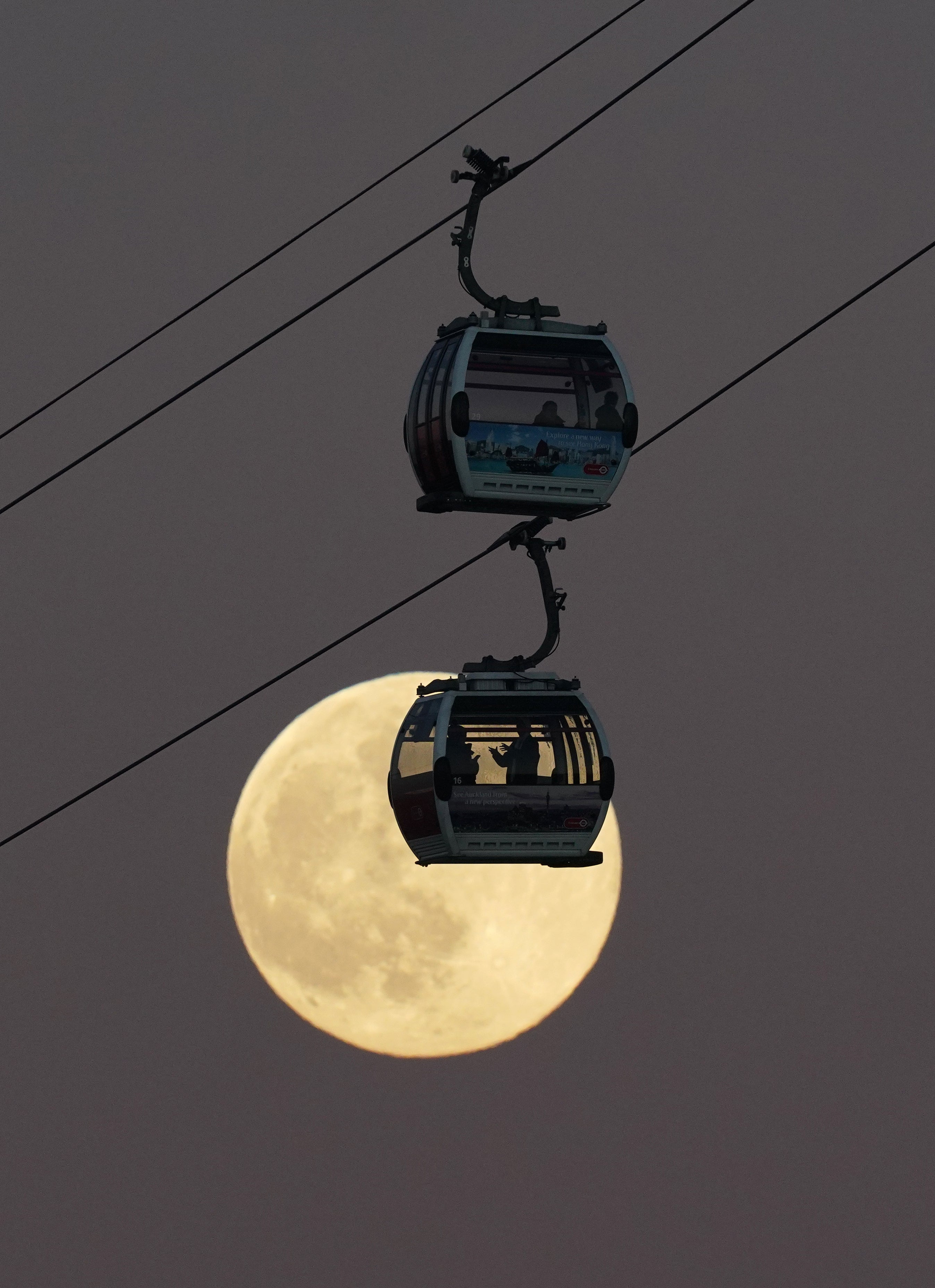 Cable cars pass in front of the moon as they cross the River Thames