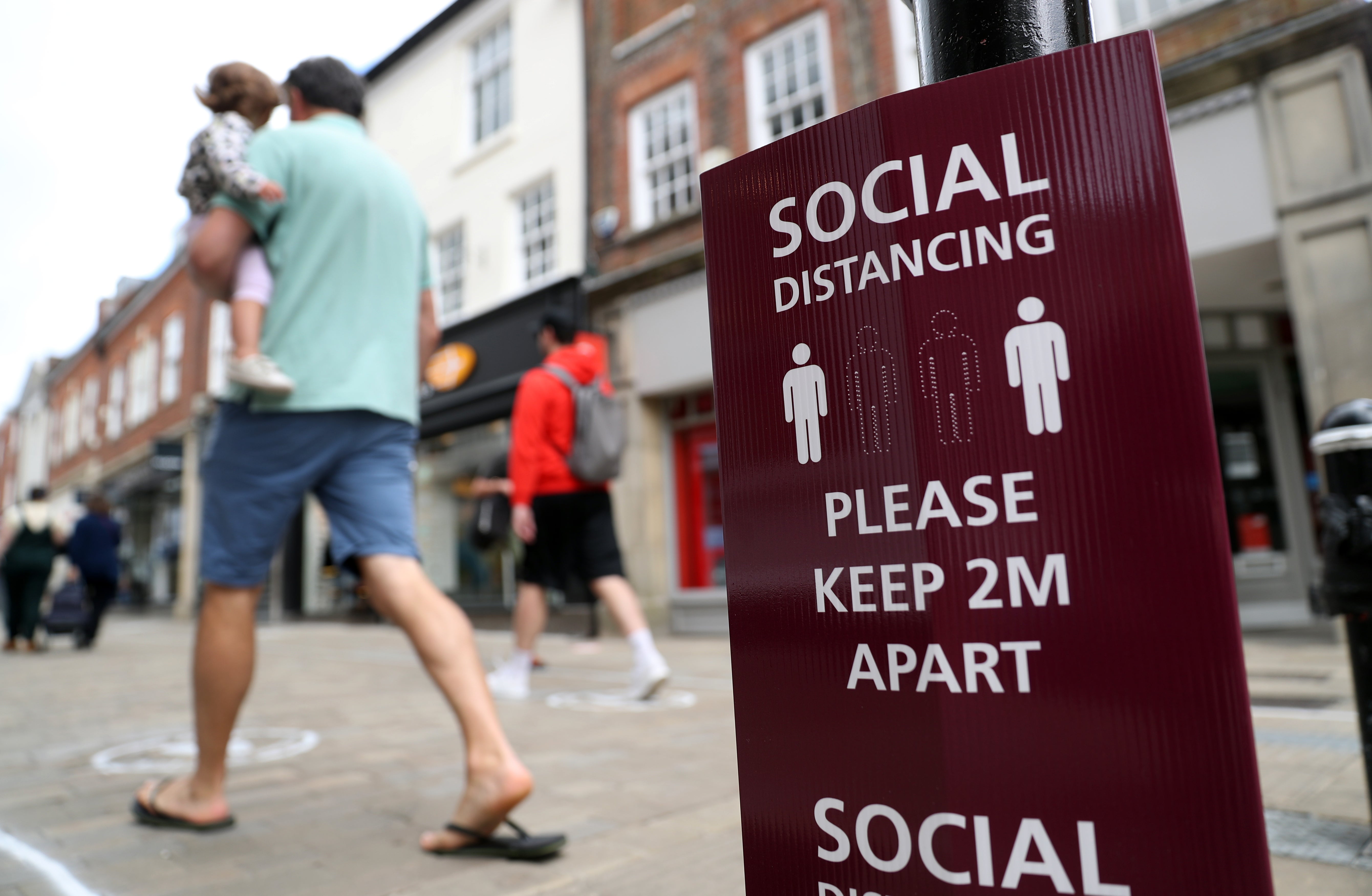 People walk past a social distancing sign on the high street in Winchester (Andrew Matthews/PA)