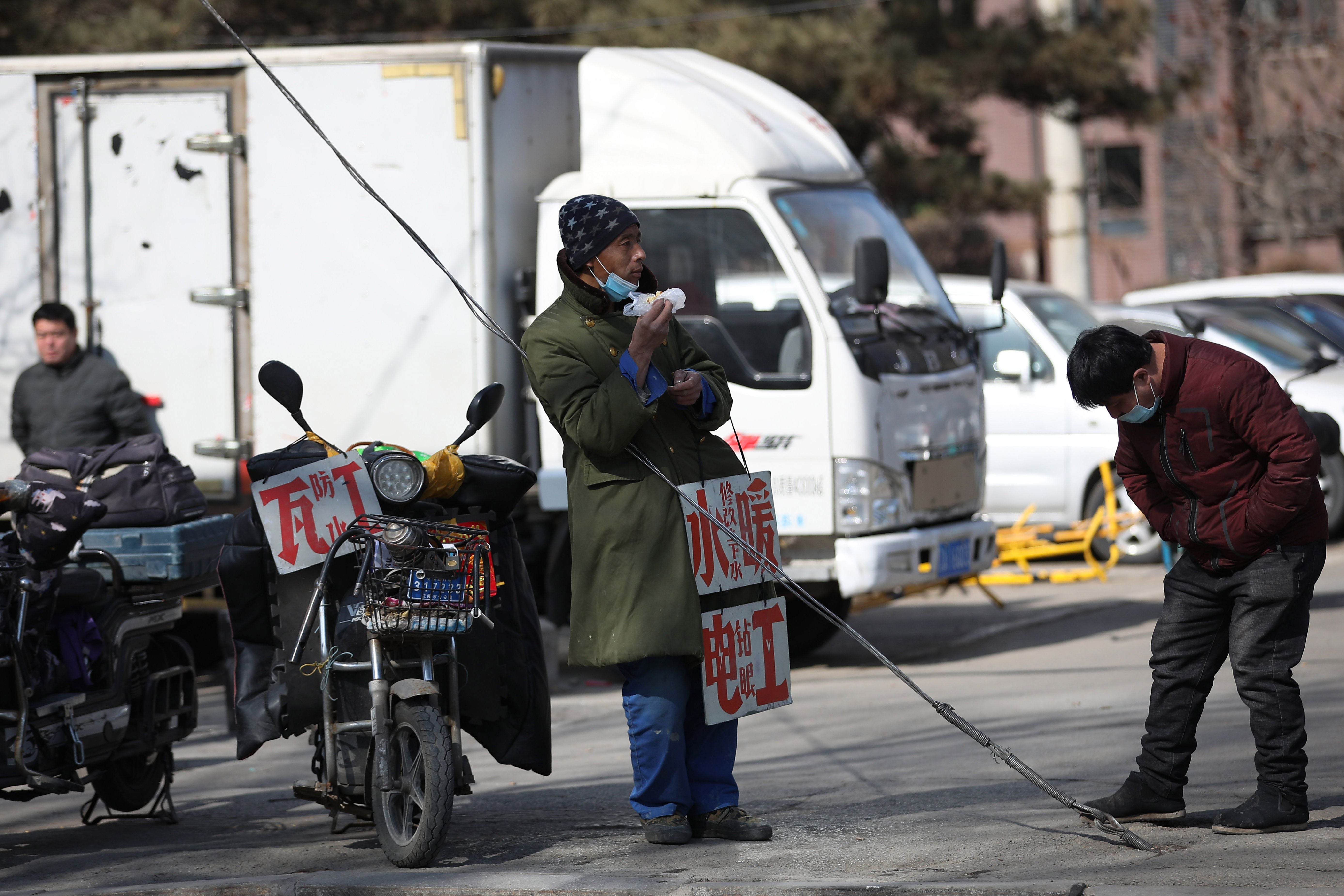 File photo: A migrant worker stands with signs advertising his work skills on a street as he waits to get hired in Shenyang, China, 25 February 2021