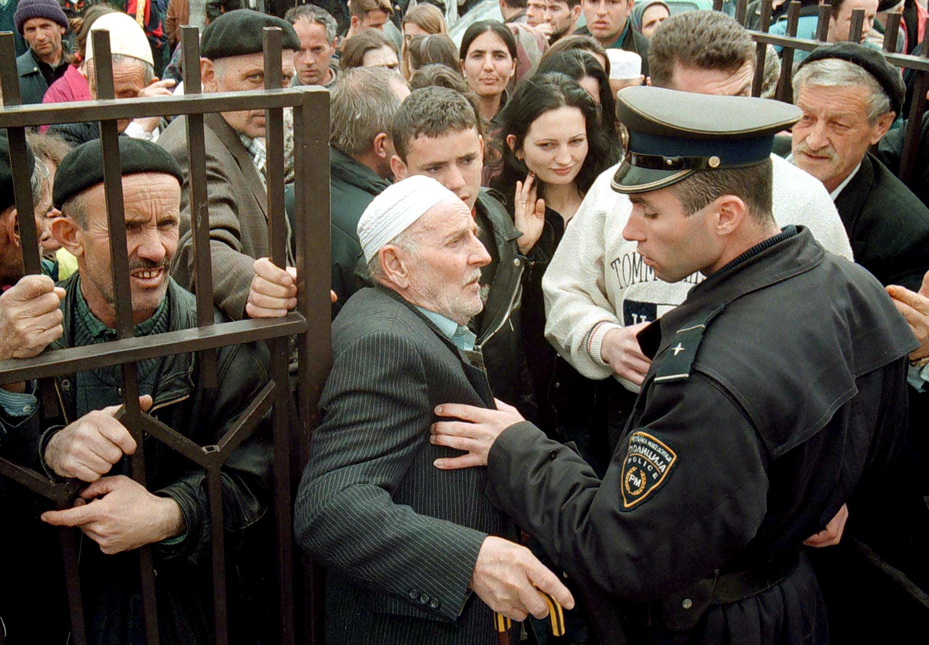 A policeman tries to push back an elderly man as ethnic Albanian refugees wait to be registered as refugees at a police station in Skopje, 23 March 1999, after fleeing from Kosovo