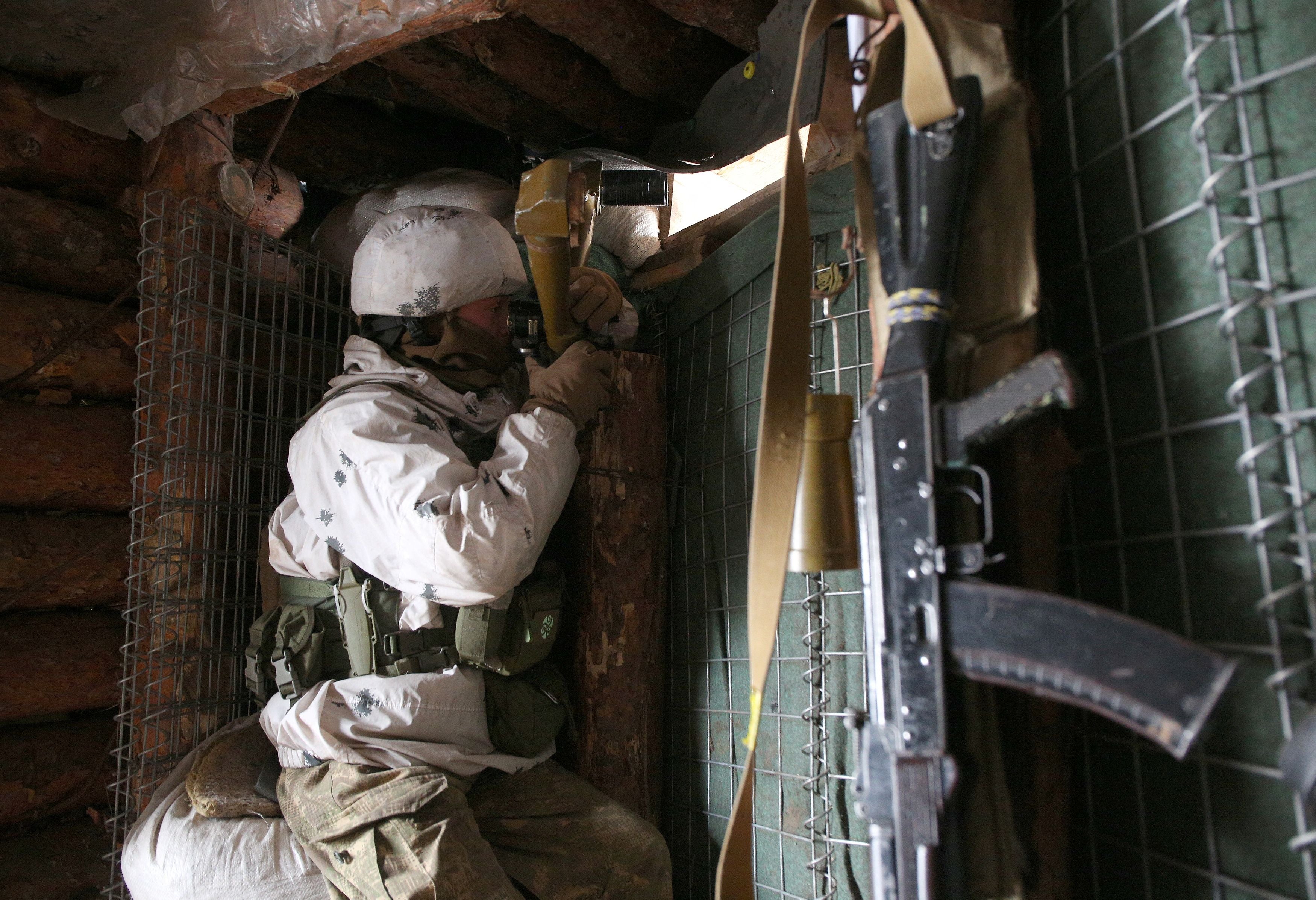 An Ukrainian Military Forces serviceman, watches through spyglass in a dugout on the frontline with Russia-backed separatists near Gorlivka, Donetsk region