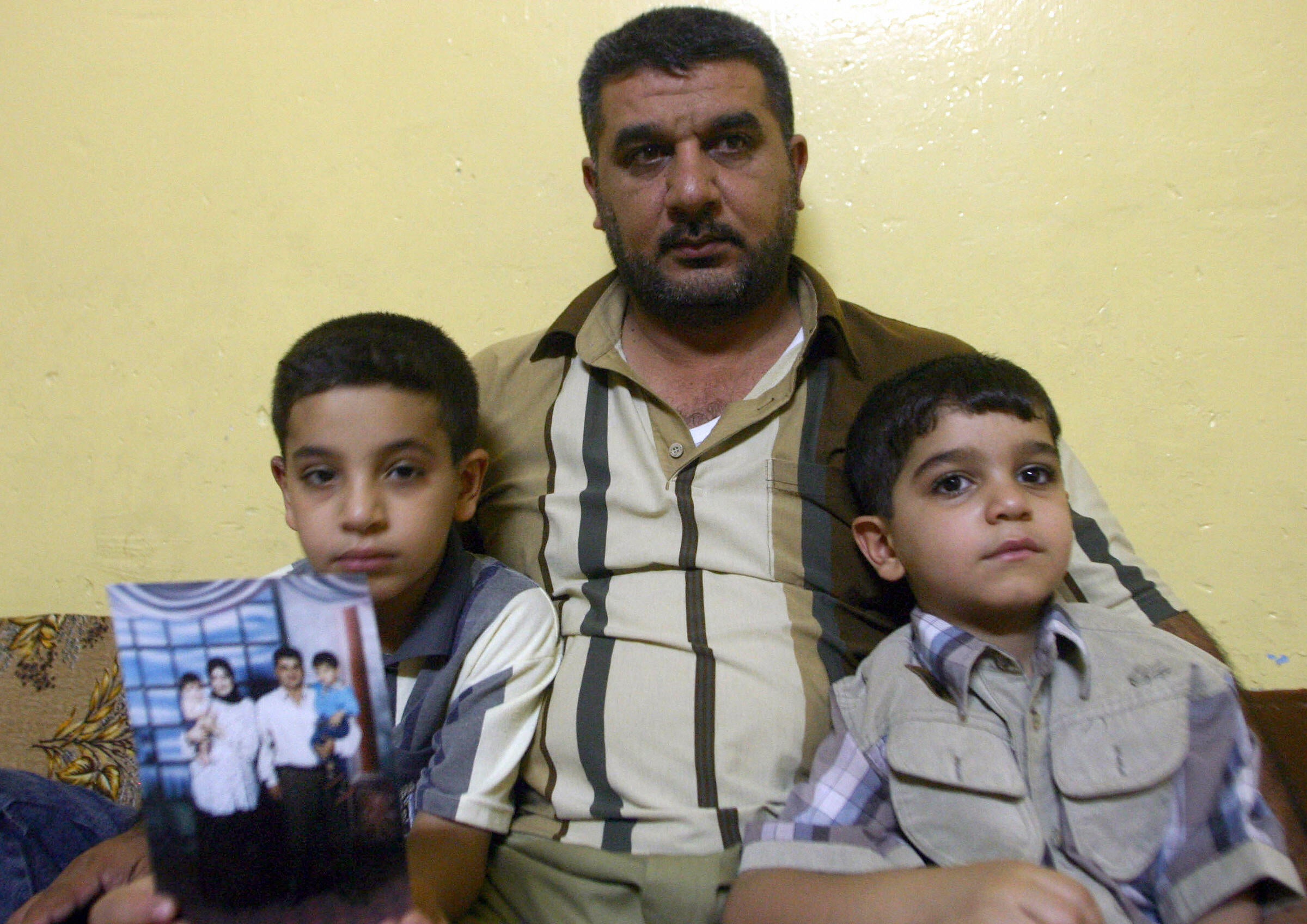 Hassan holds a family photo as he sits with his uncle, Alaa, and his younger brother Ali at their home in Basra. Their father, Baha Mousa, was killed in custody