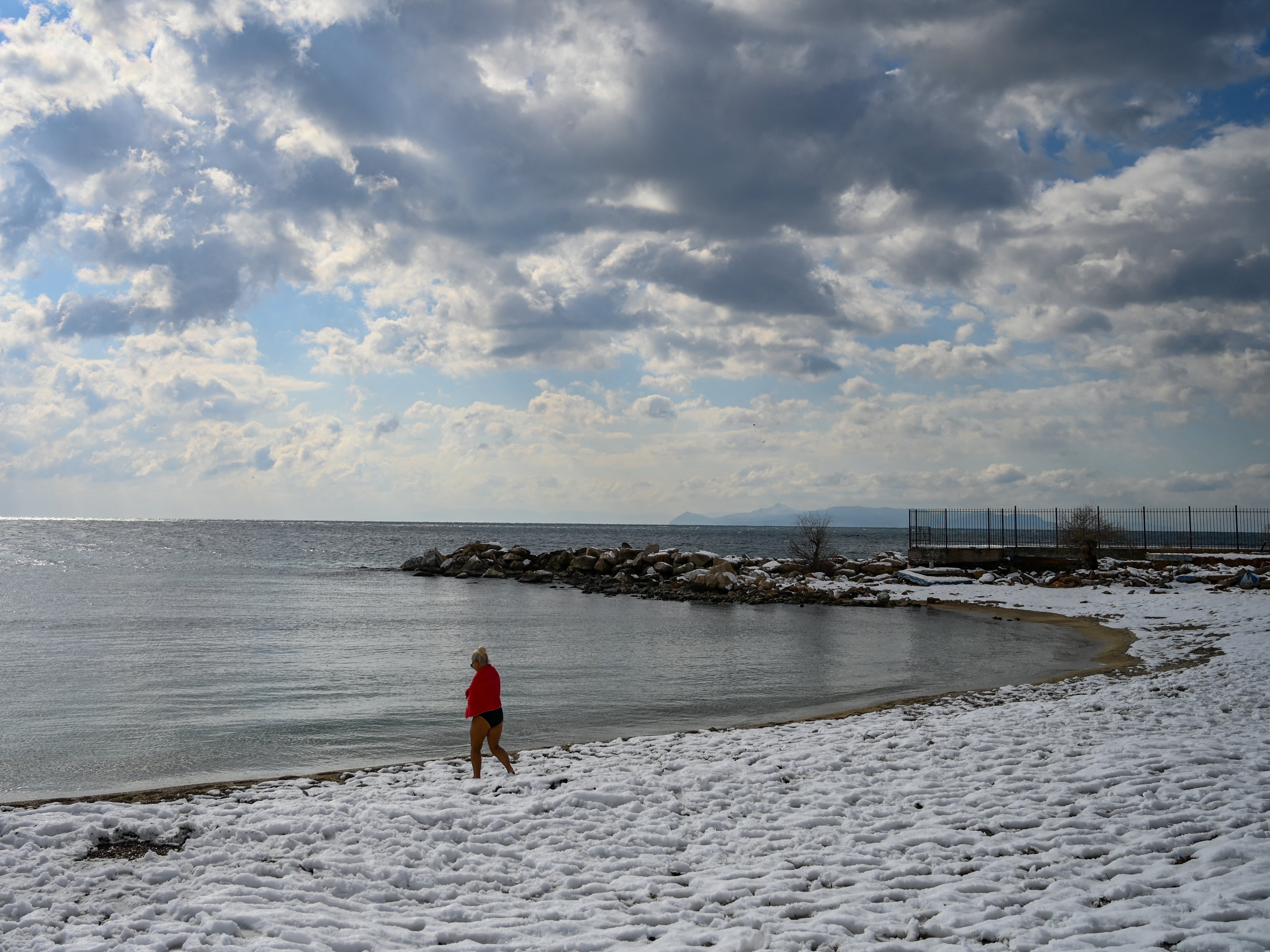 A swimmer walks on a snow covered beach after a heavy snowfall in Athens