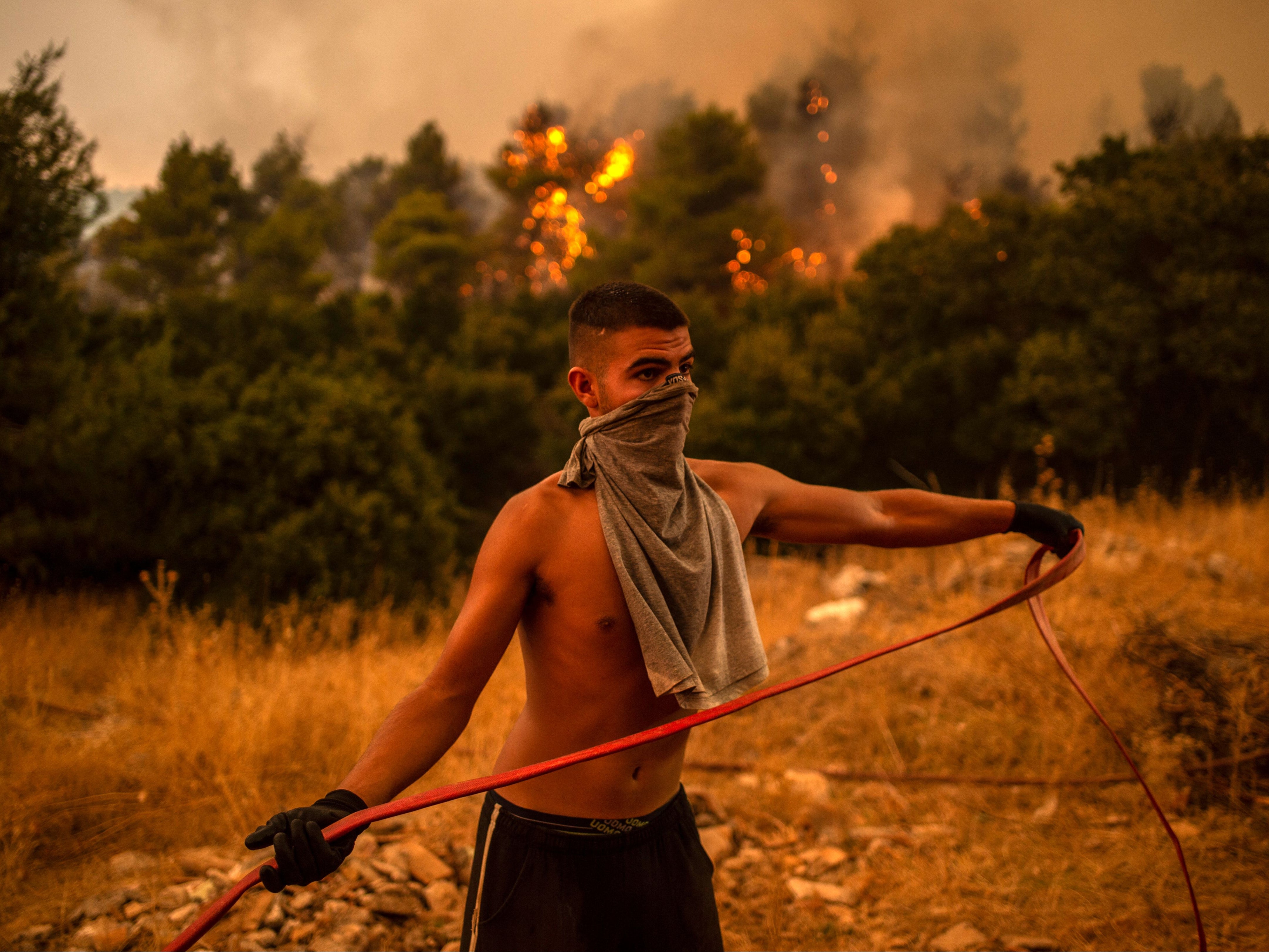 A volunteer holds a water hose during efforts to try to extinguish a fire in the village of Villa, north of Athens