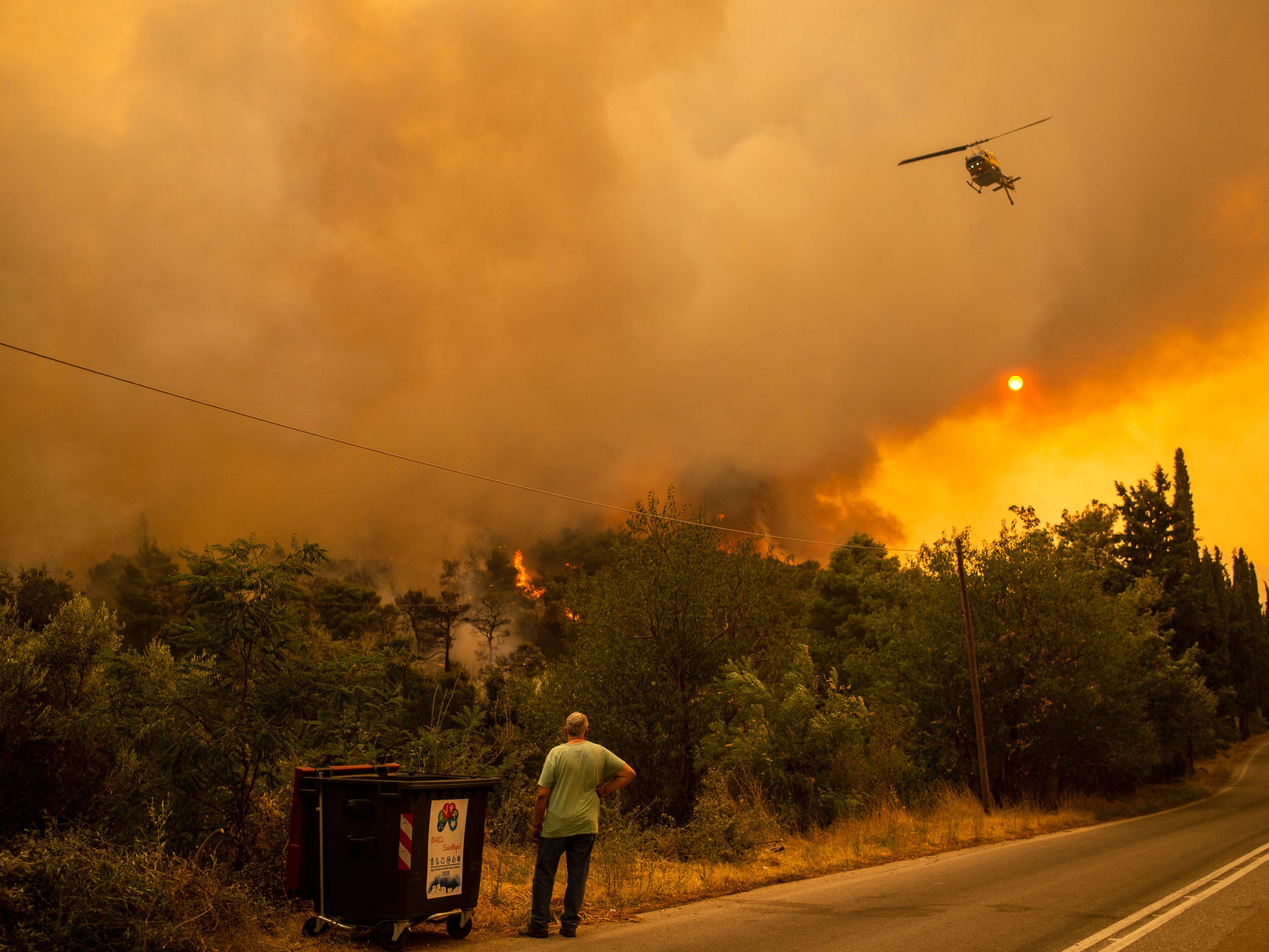 A man watches a helicopter during a fire in the village of Villa, northwestern Athens