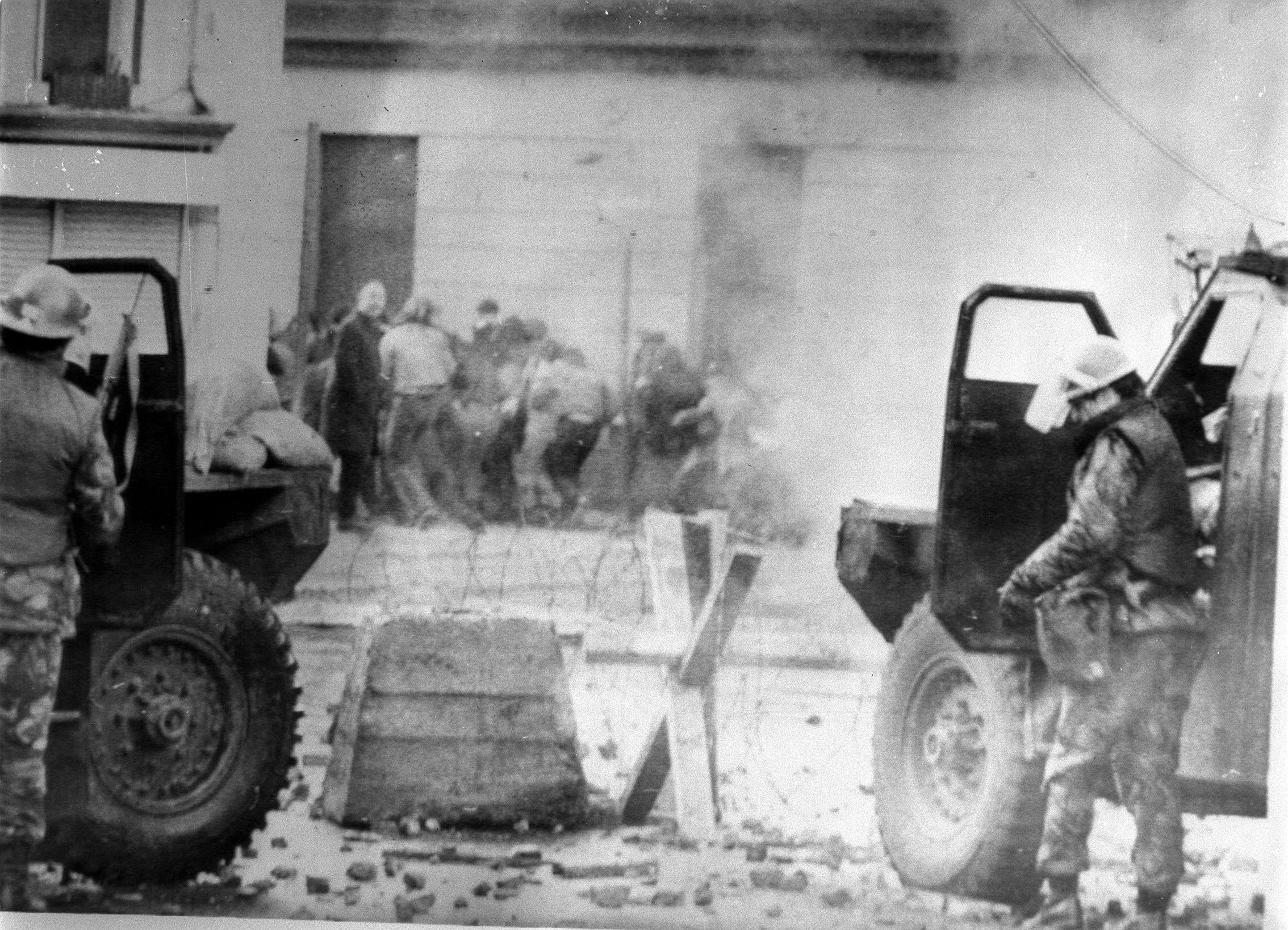 Soldiers take cover behind their armoured cars while dispersing rioters with CS gas in Londonderry (PA)