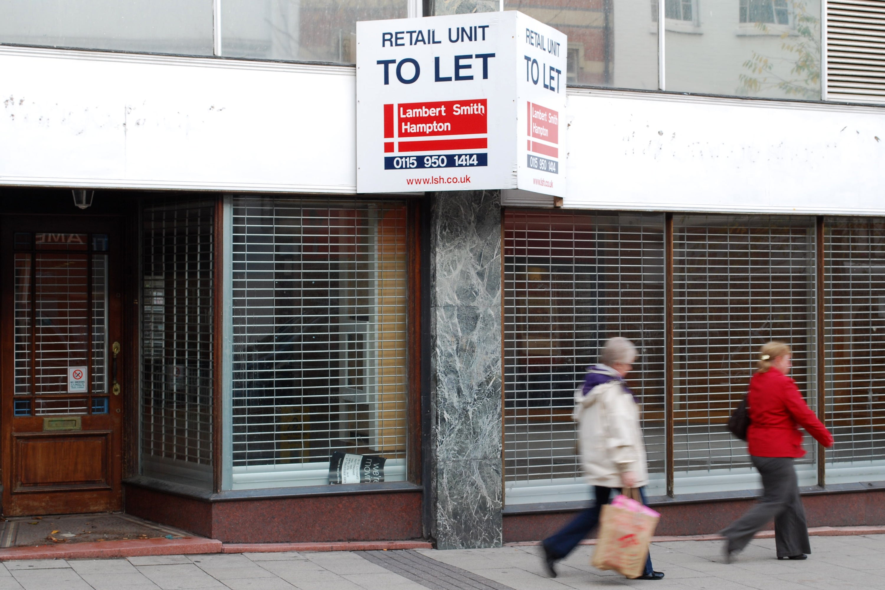 Pedestrians walk past an empty shop unit