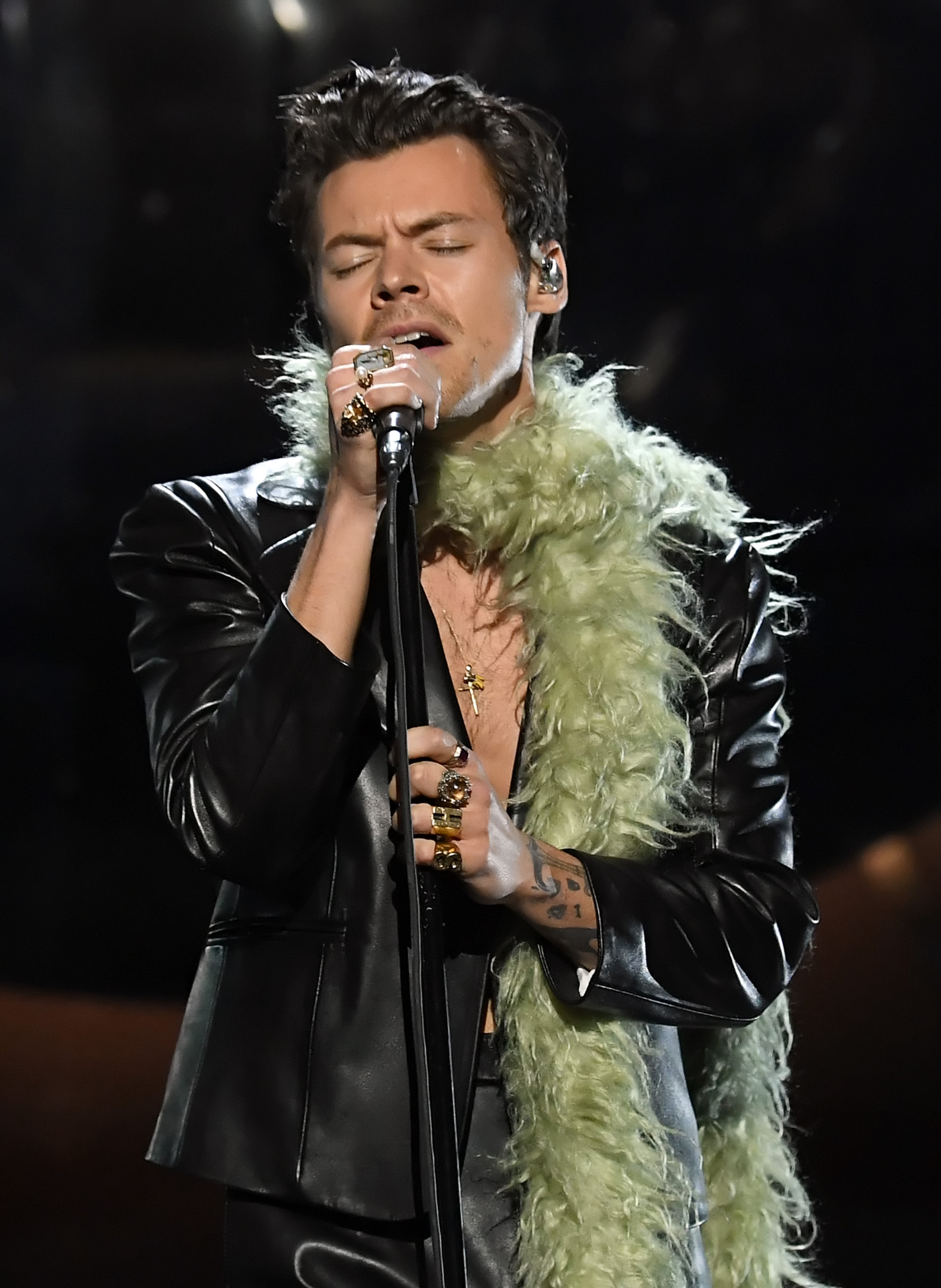 Styles performing at the Grammys wearing a leather suit, no shirt, and a green feather boa