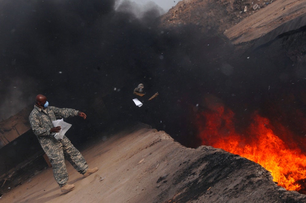 A US servicemember tosses trash into a burn pit