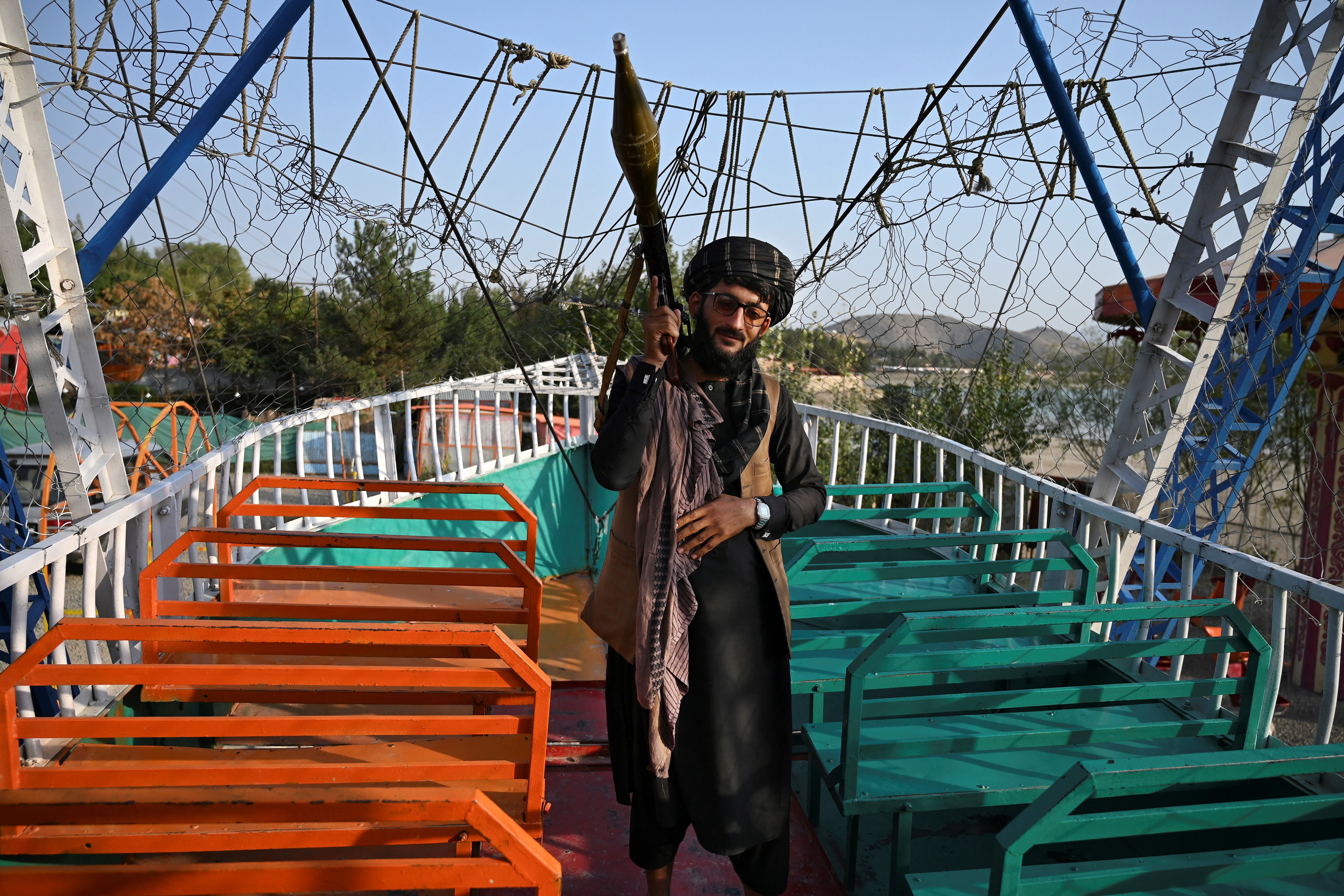 A Taliban fighter carrying a rocket propelled grenade (RPG) launcher stands on pirate ship ride in a fairground at Qargha Lake on the outskirts of Kabul, 28 September 2021