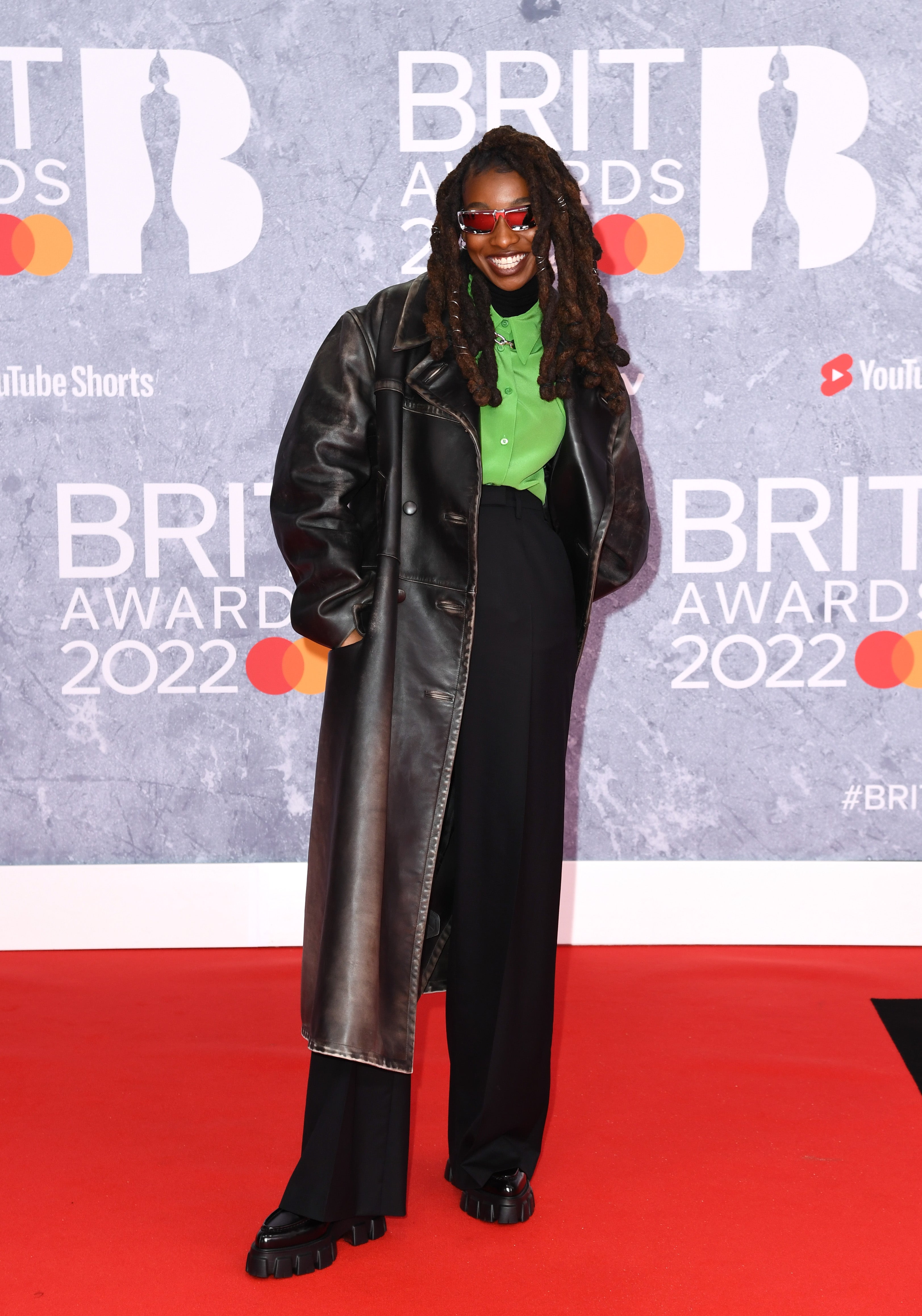 The rapper wore a pair of black high-waisted trousers with a bright lime green collared shirt over the top of a black poloneck top. Little Simz paired the look with a long black leather coat, red-tinted sunglasses and a pair of chunky-soled shoes.