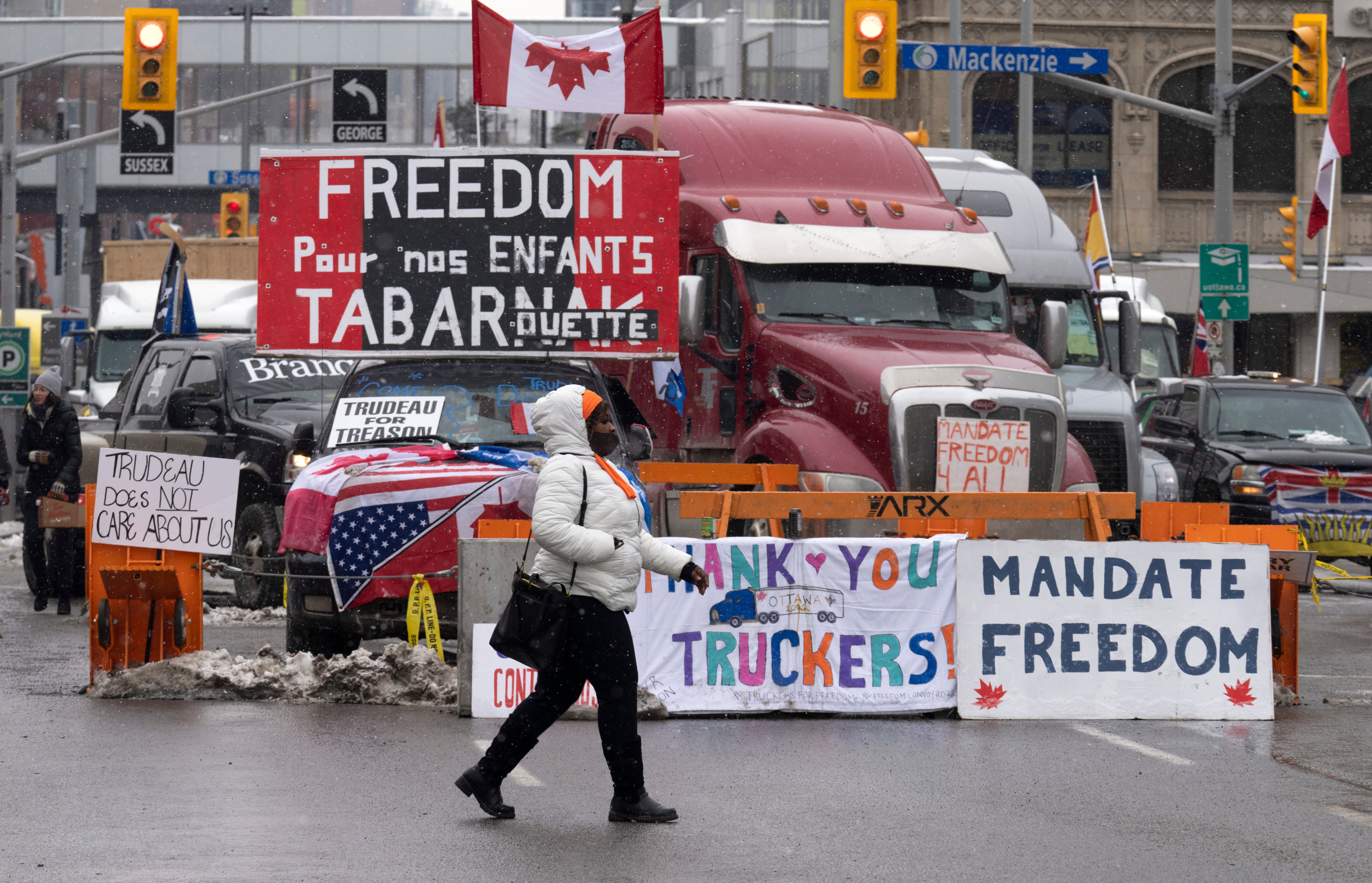 A woman crosses the street in front of vehicles parked as part of the trucker protest, Tuesday, Feb. 8, 2022 in Ottawa.