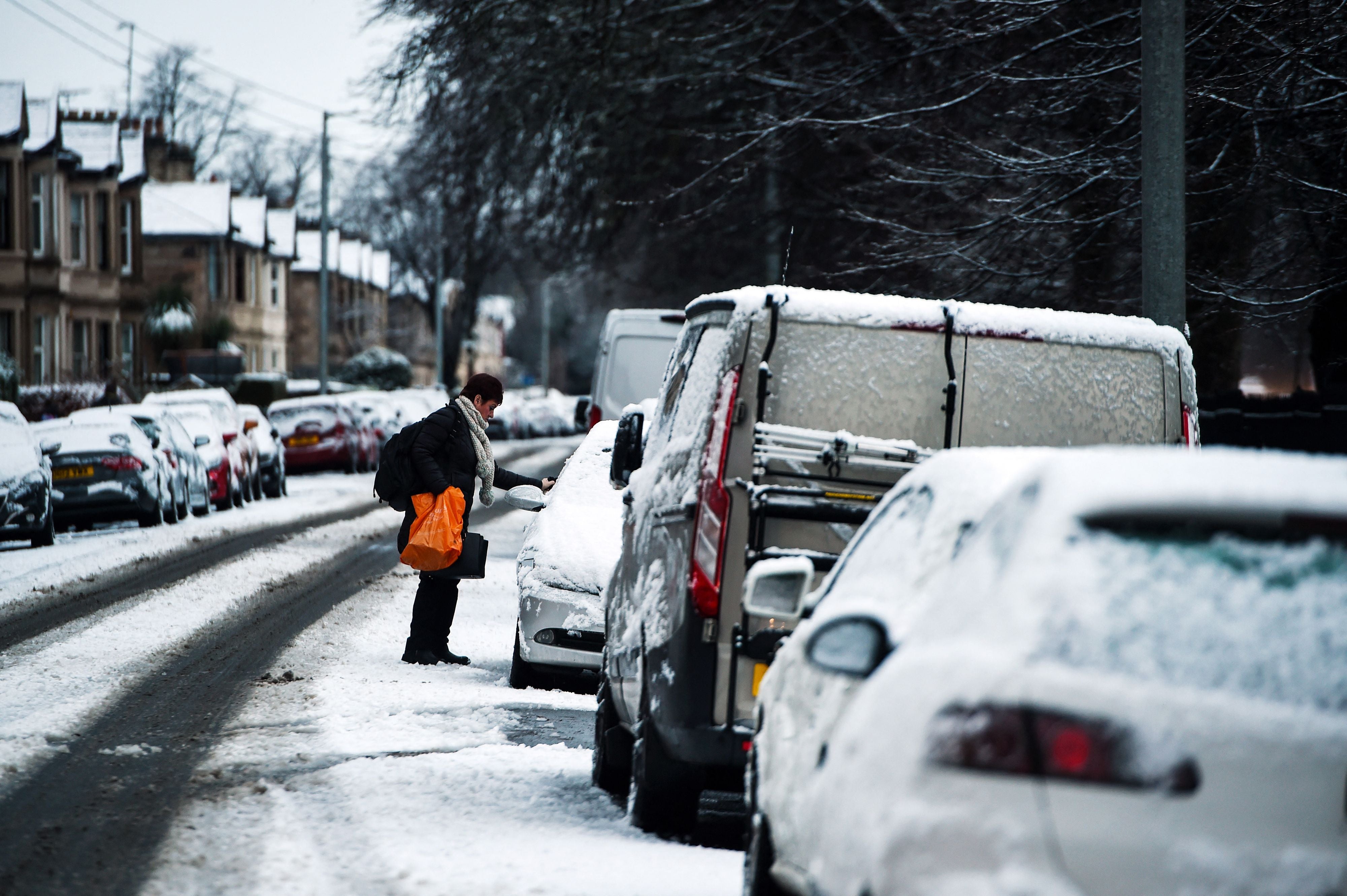 A person clears the snow from the windows of their car in Whiteinch, in the West End of Glasgow