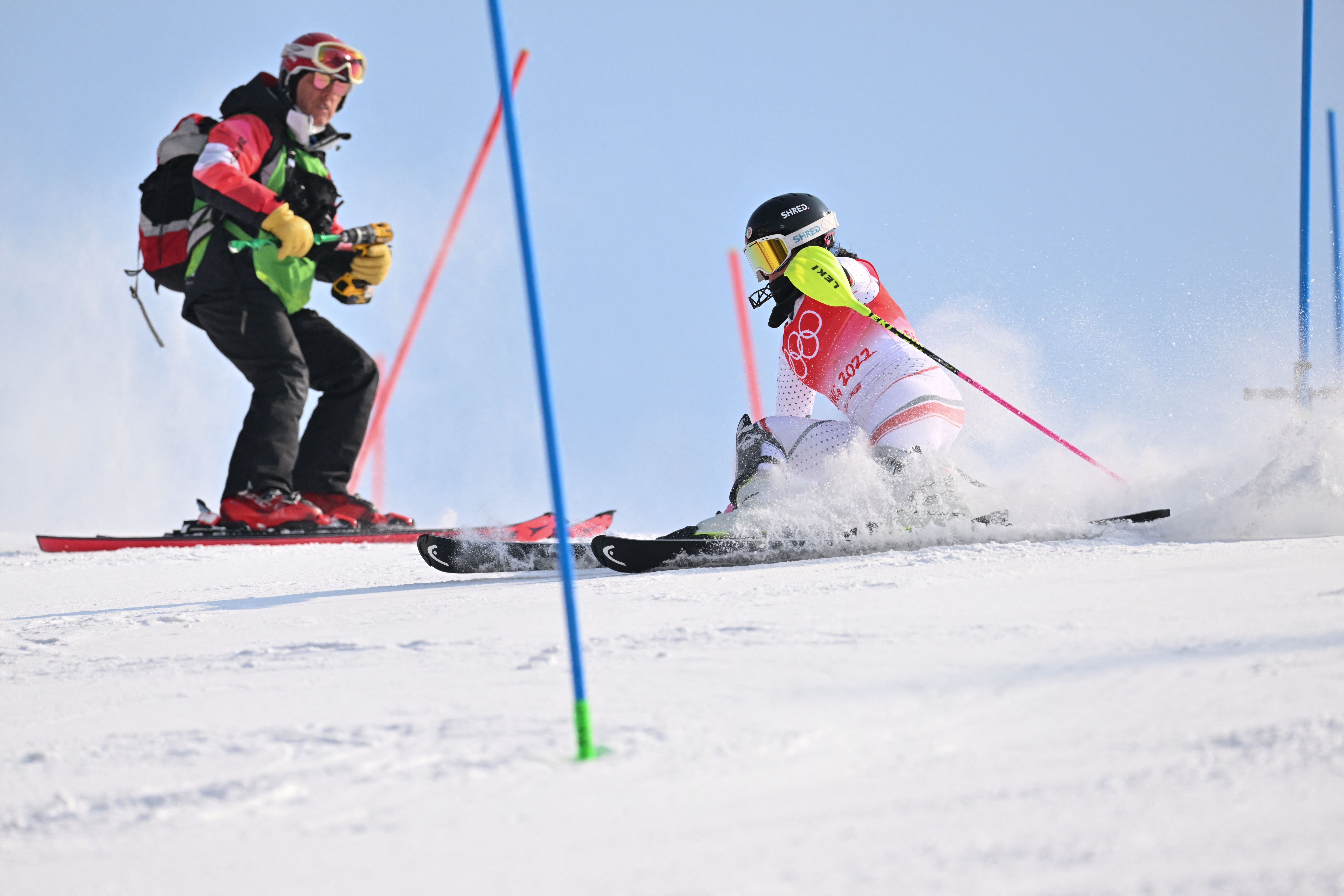 Bulgaria's Eva Vukadinova (R) reacts as a technician is still on the course after leaving a tool on the pole during the first run of the women's slalom during the Beijing 2022 Winter Olympic Games