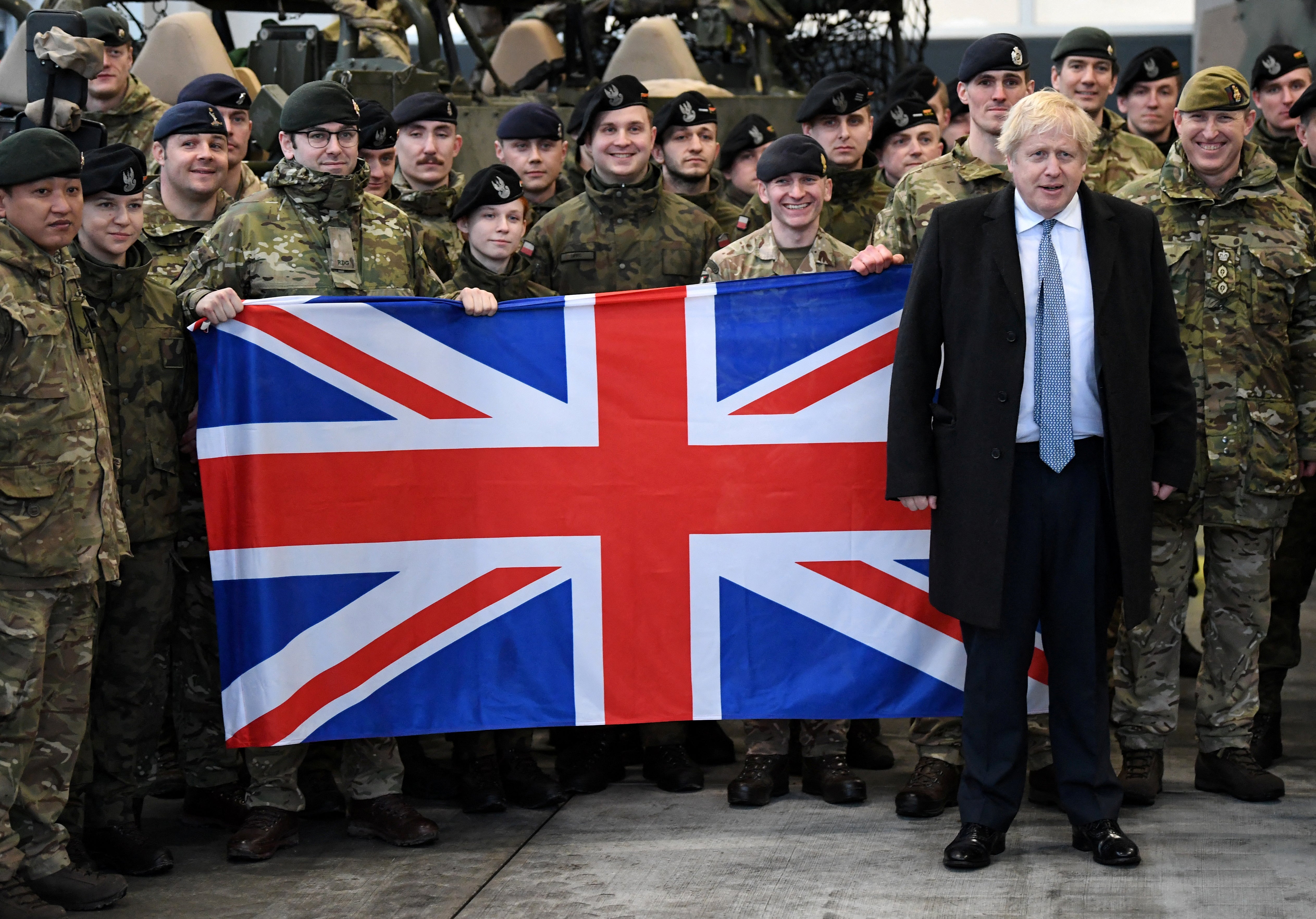 Boris Johnson poses for a photograph with British troops in front of a Union flag during a visit to Warszawska Brygada Pancerna military base near Warsaw