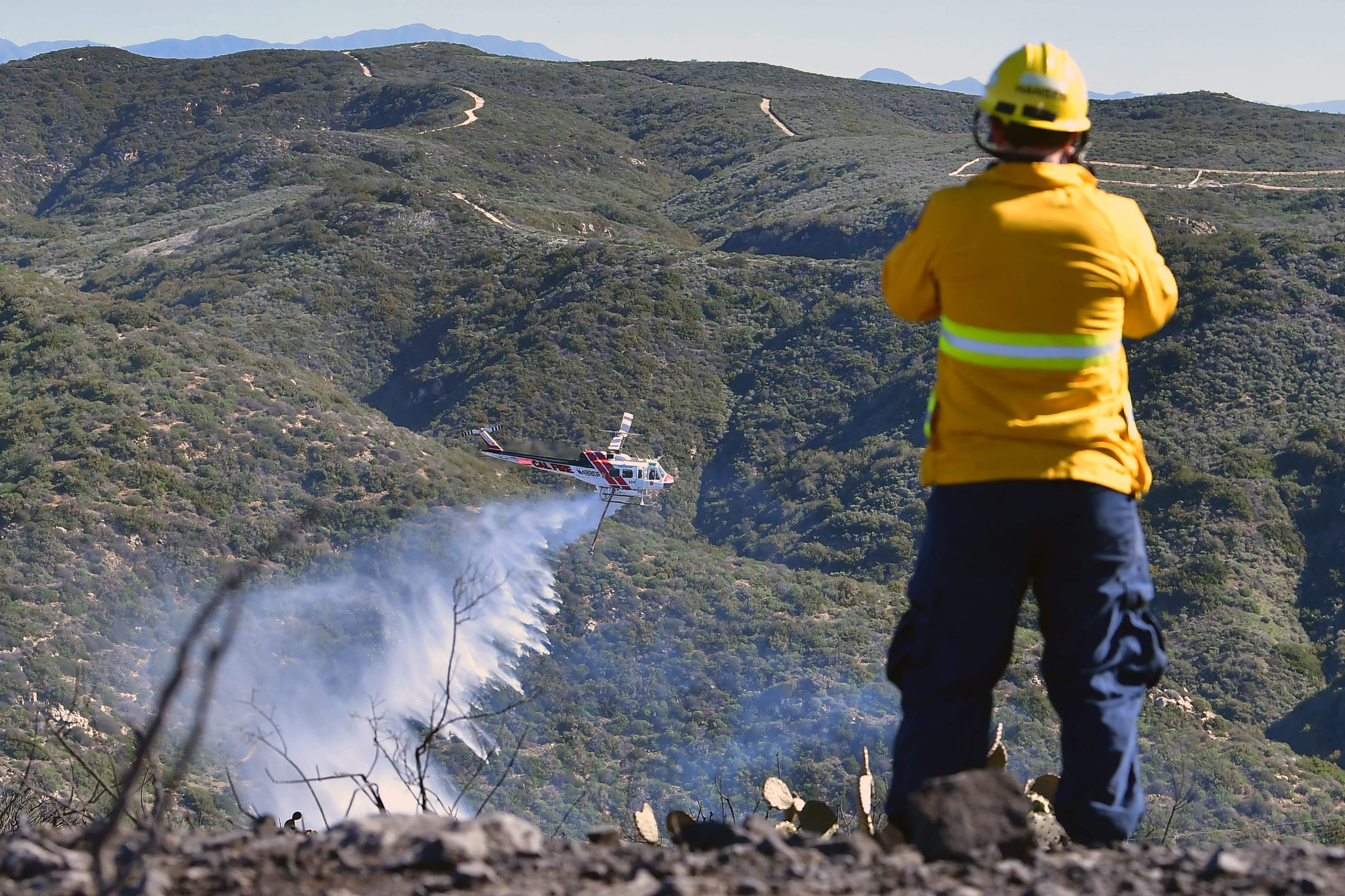 A firefighter watches as a helicopter dumps water onto flames from the Emerald Fire