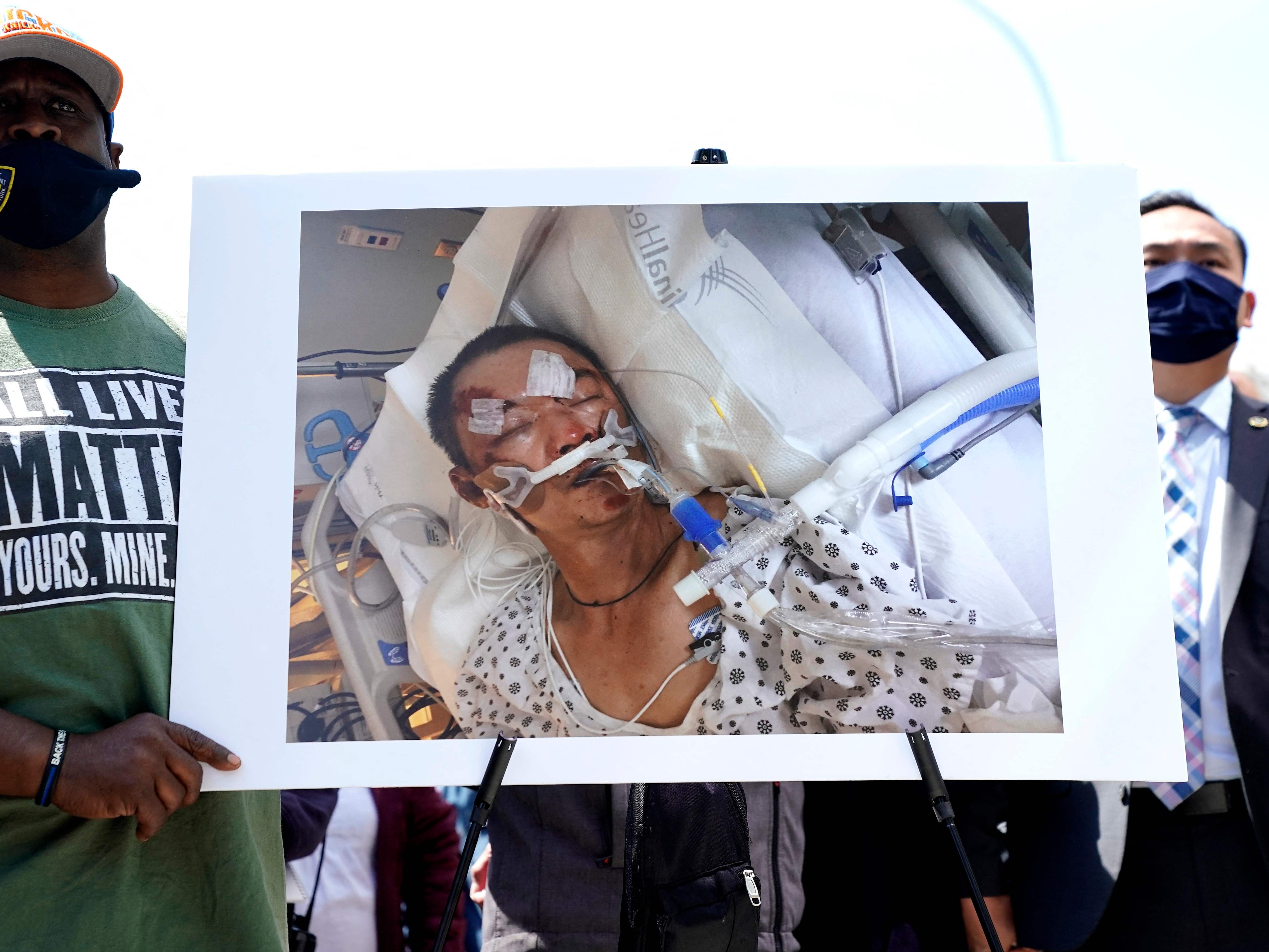 People hold a photo of 61-year old Yao Pan Ma who was was attacked from behind, pushed to the ground, and repeatedly kicked in Harlem