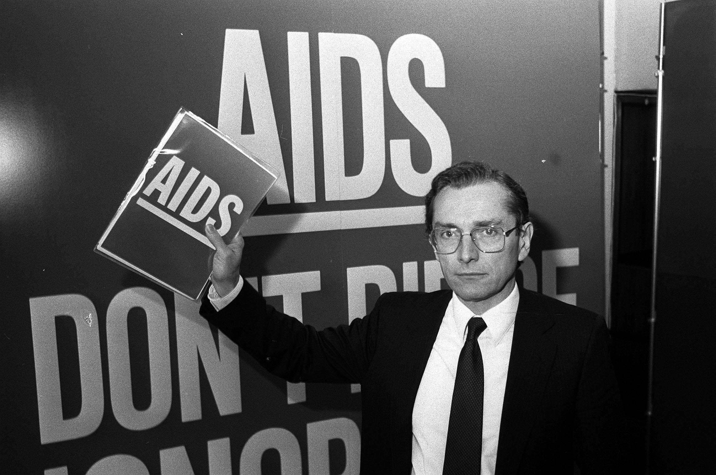 Health secretary Norman Fowler in front of a poster reading ‘Aids Don’t Die of Ignorance’