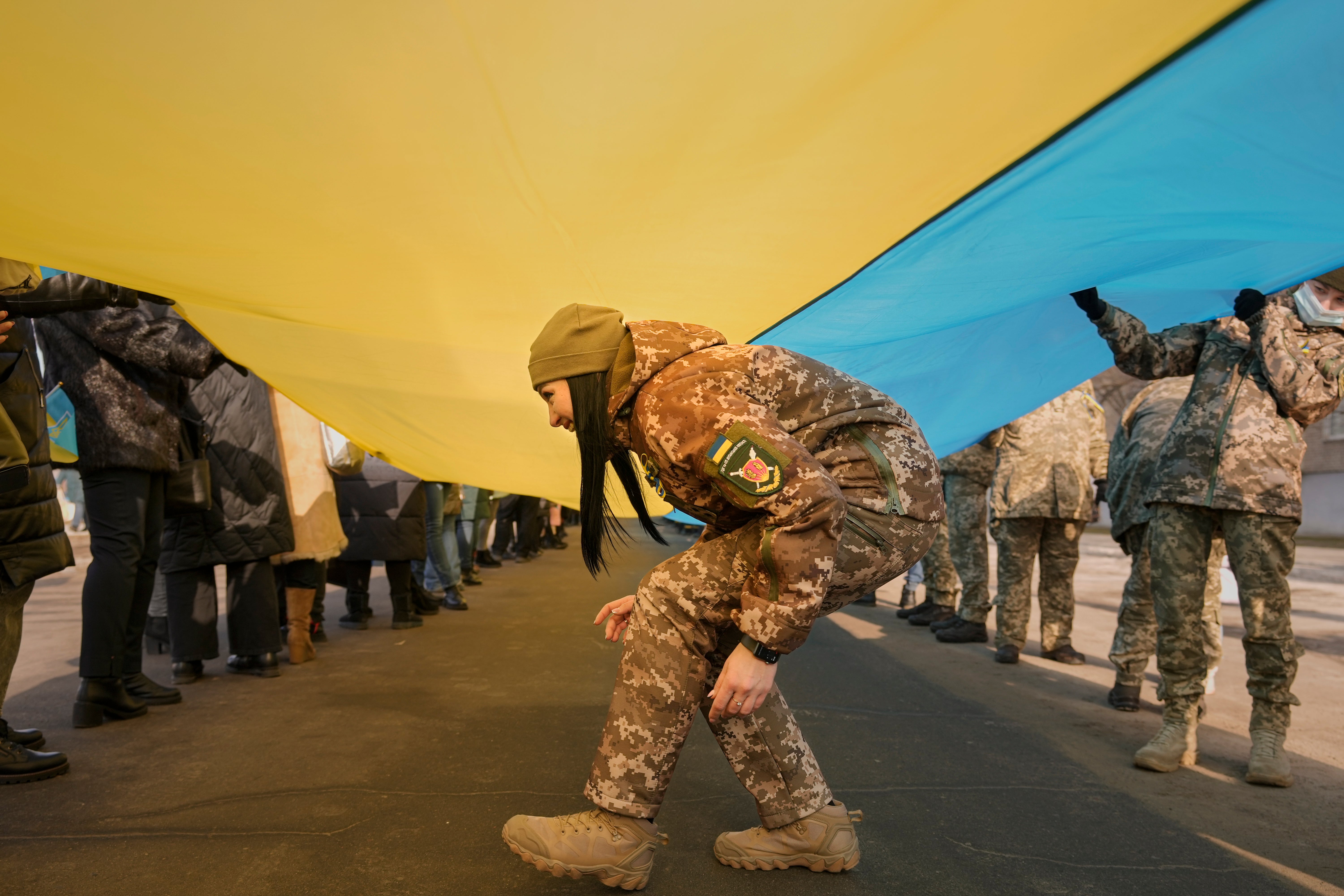 A Ukrainian servicewoman walks under a large Ukrainian flag carried by people marking a Day of Unity in Sievierodonetsk