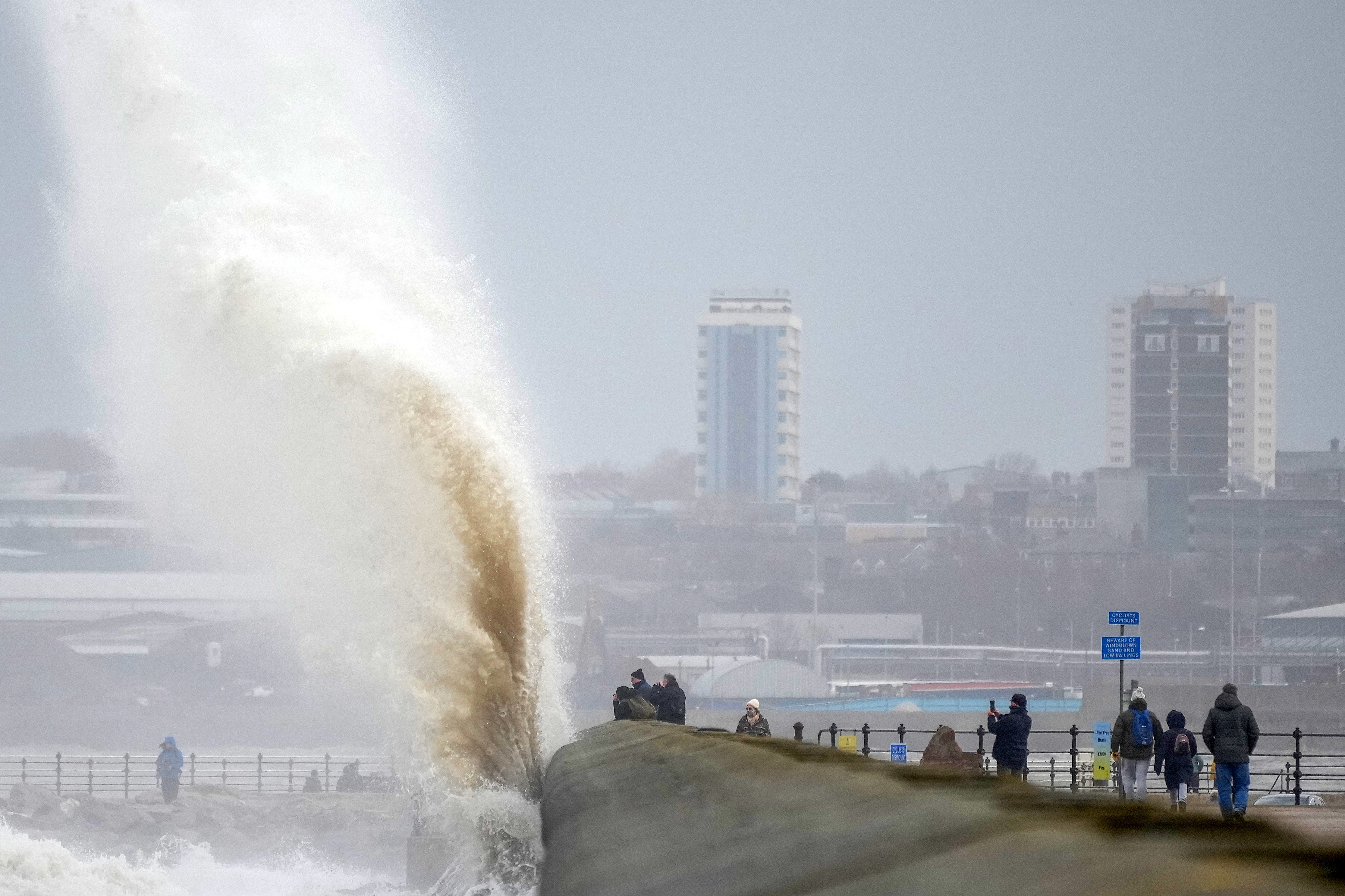 People view the waves created by high winds and spring tides hitting the sea wall at New Brighton promenade